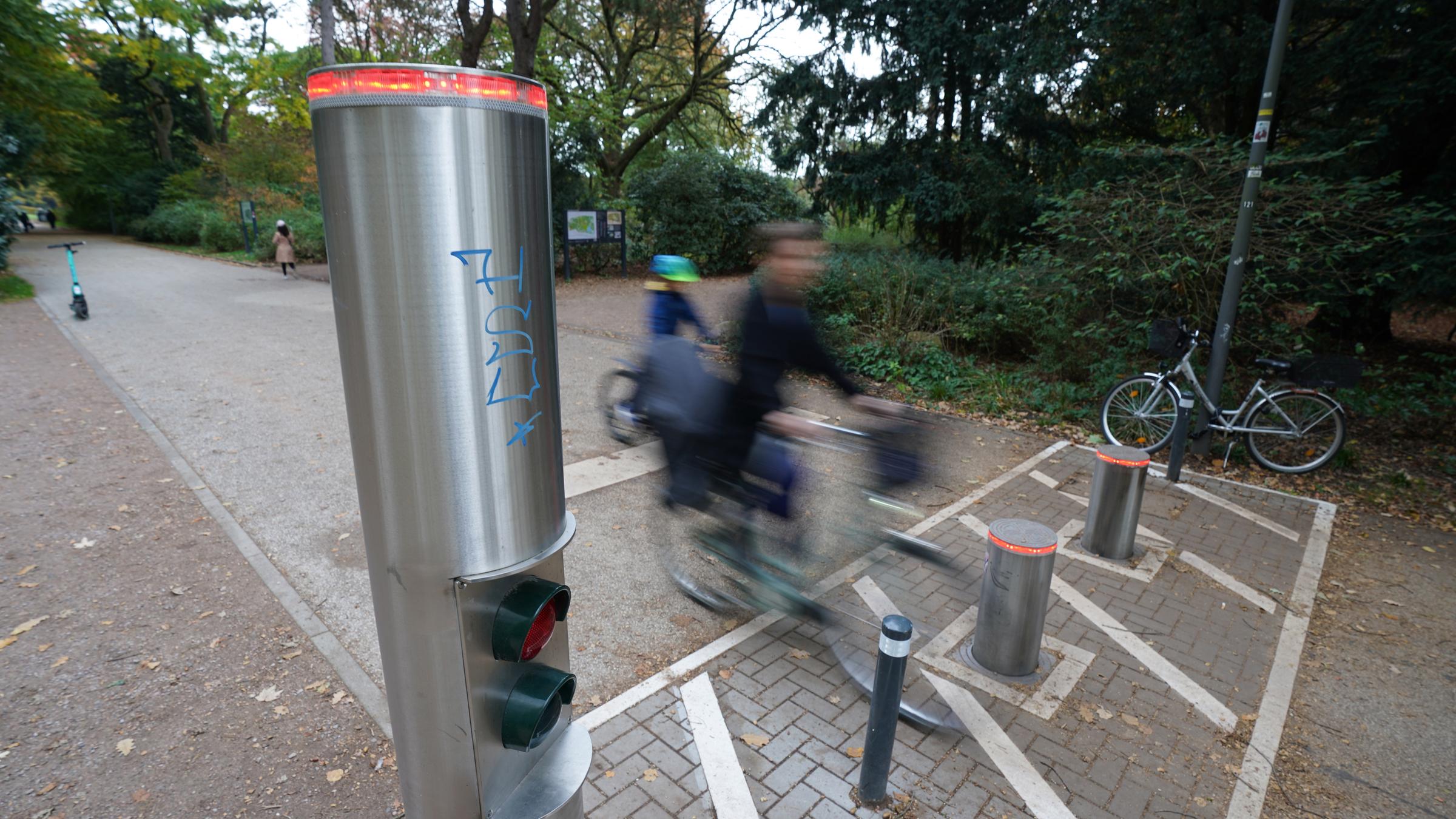 Passanten fahren auf Fahrrädern an einer Poller-Anlage im Stadtpark vorbei. Im Stadtpark wurde eine einfache Schranke durch die Poller-Anlage ersetzt. Seitdem war sie mehr als vier Jahre außer Betrieb und verschlang rund 35.000 Euro für Reparatur- und Wartungsarbeiten. 