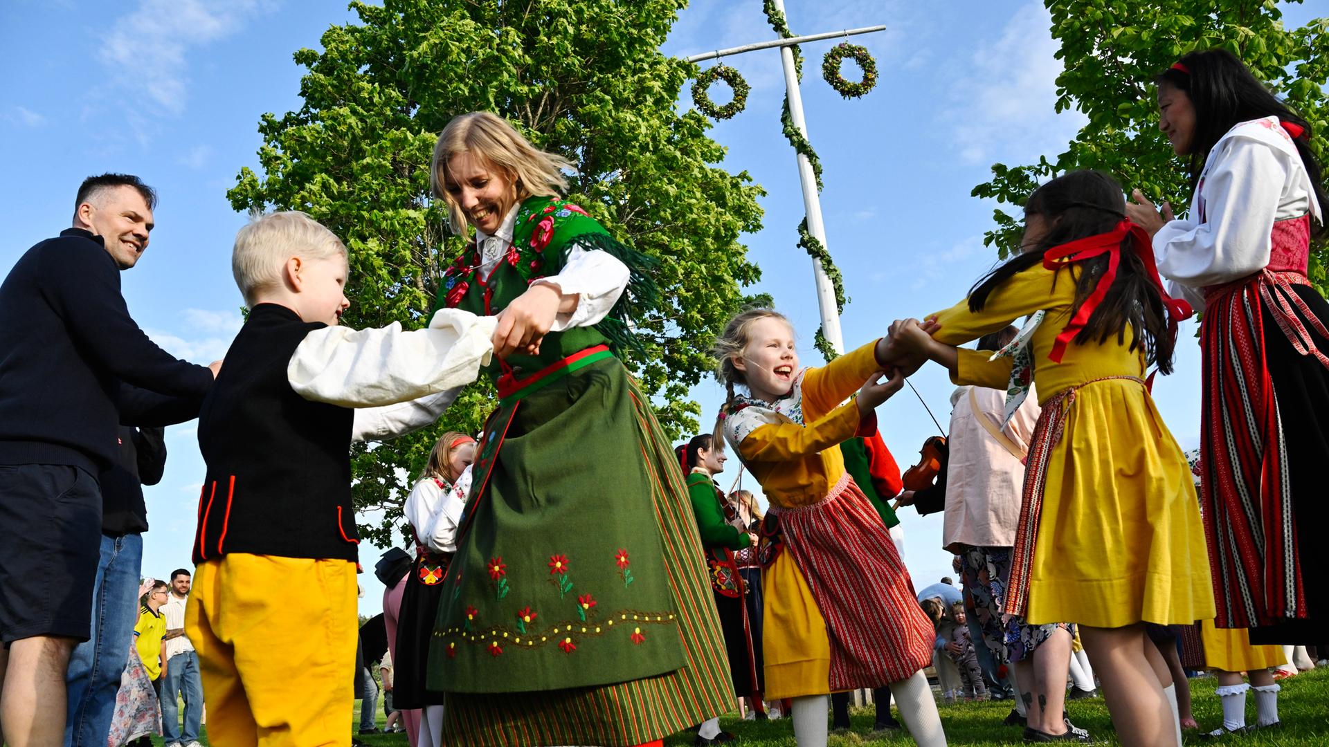 Kinder und Erwachsene tanzen den traditionelle Tanz um die Stange bei der Mittsommerfeier im schwedischen Tibble am 19.06.2025.