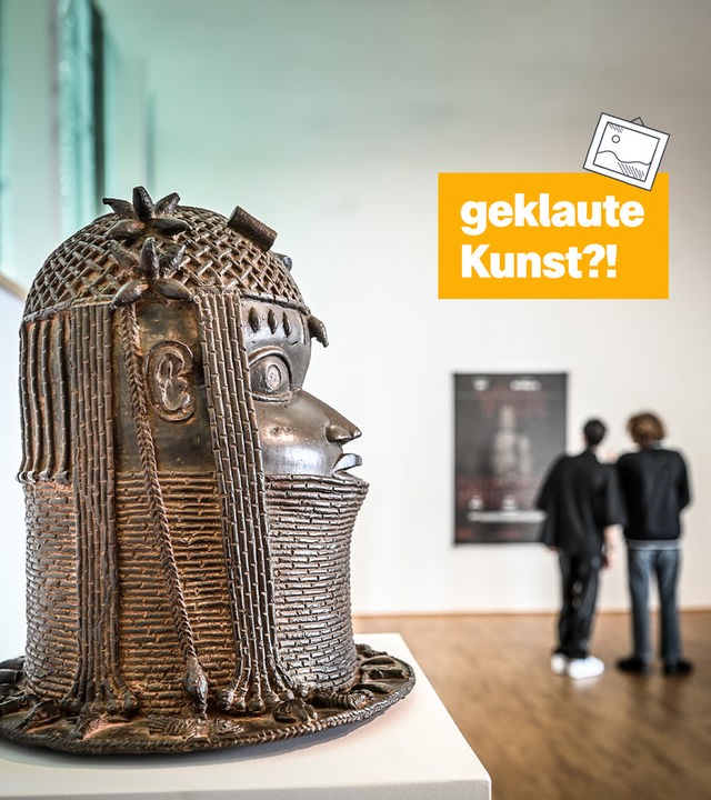 Ein Museum, in dem links einer Bronze-Skulptur eines Kopfes steht. Rechts daneben der Text: "geklaute Kunst?!"