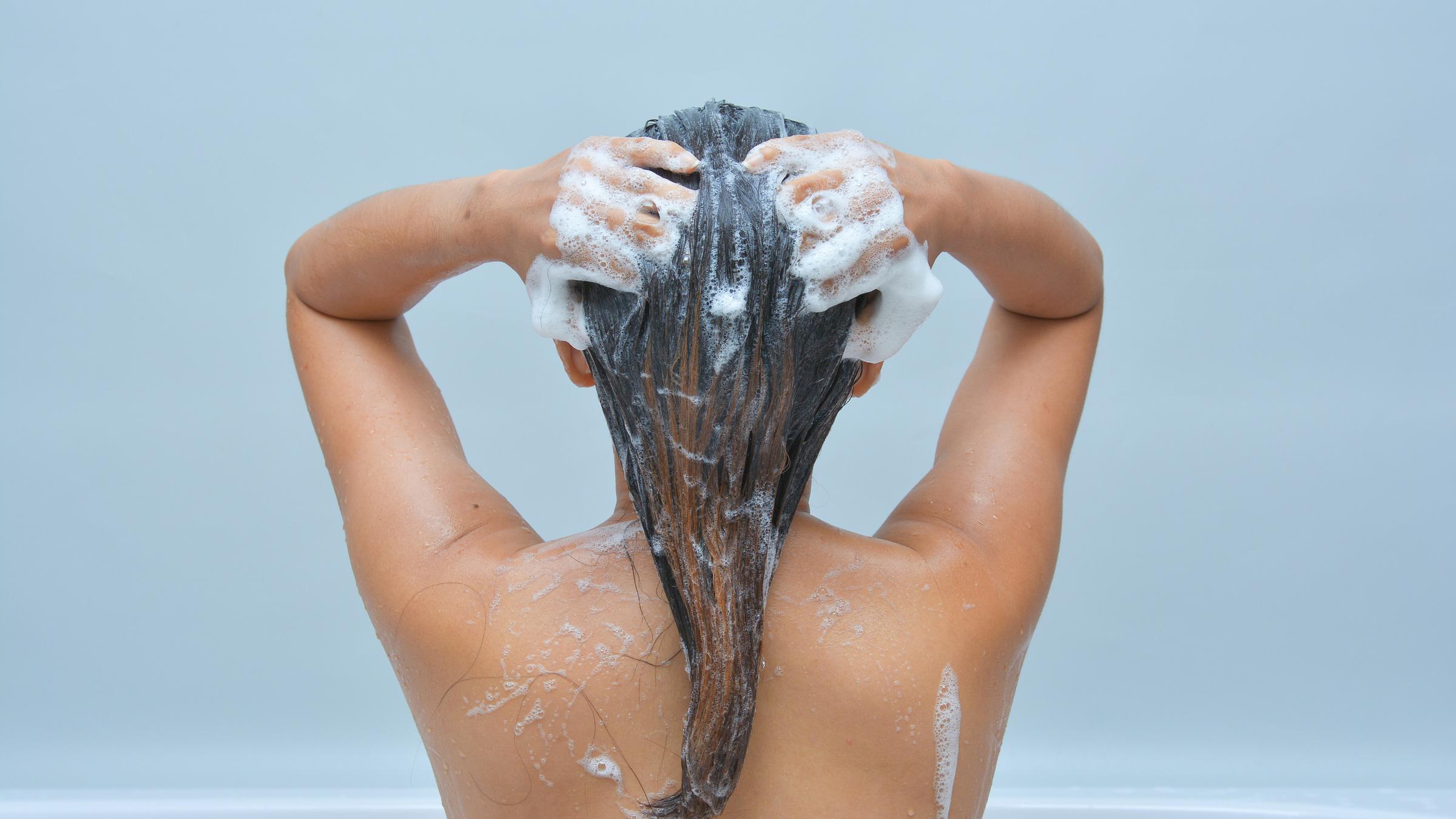 Eine Person steht unter der Dusche und schäumt sich die Haare mit Shampoo ein