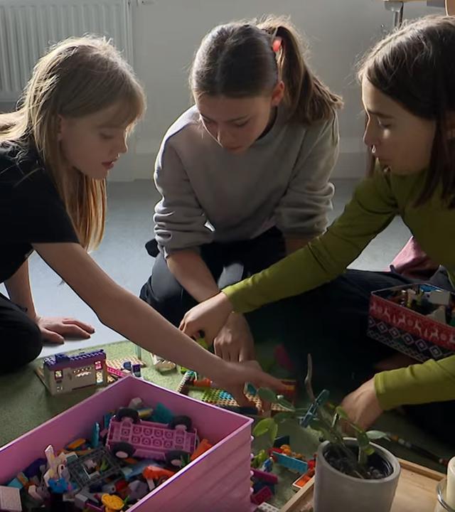 Kinder sitzen zusammen an einem Tisch, sie schreiben und sind am Laptop