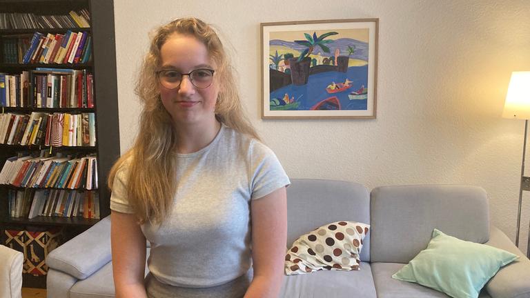 EIn Mädchen steht im Wohnzimmer und lächelt vorsichtig. 