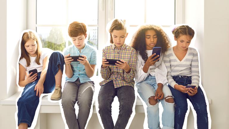 Kinder sitzen nebeneinander auf einer Fensterbank und sind am Handy