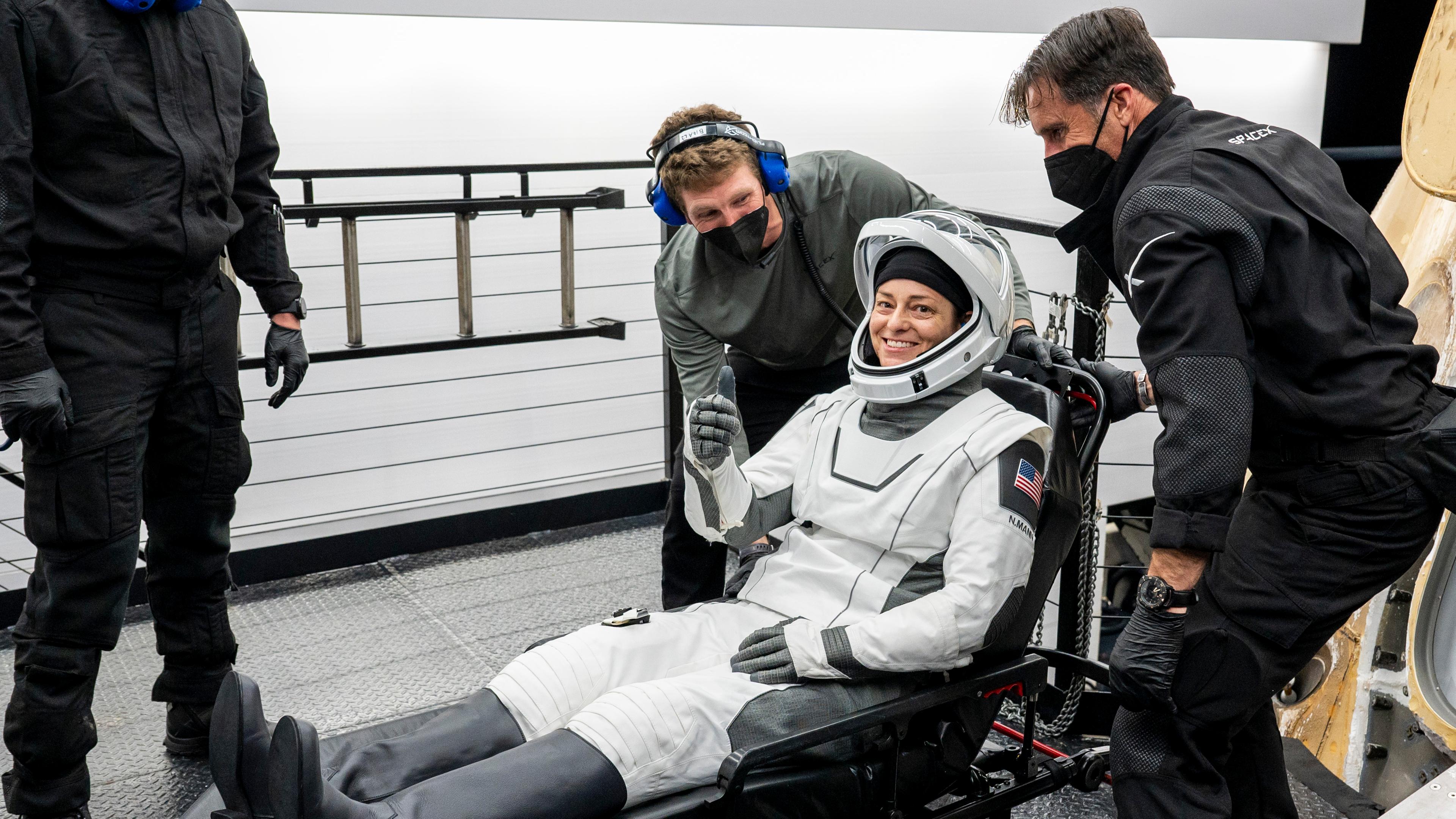 NASA-Astronautin Nicole Mann streckt den Daumen nach oben. Sie wird von mehreren SpaceX-Mitarbeitern auf einer Trage sitzend aus einer Raumkapsel geholt.