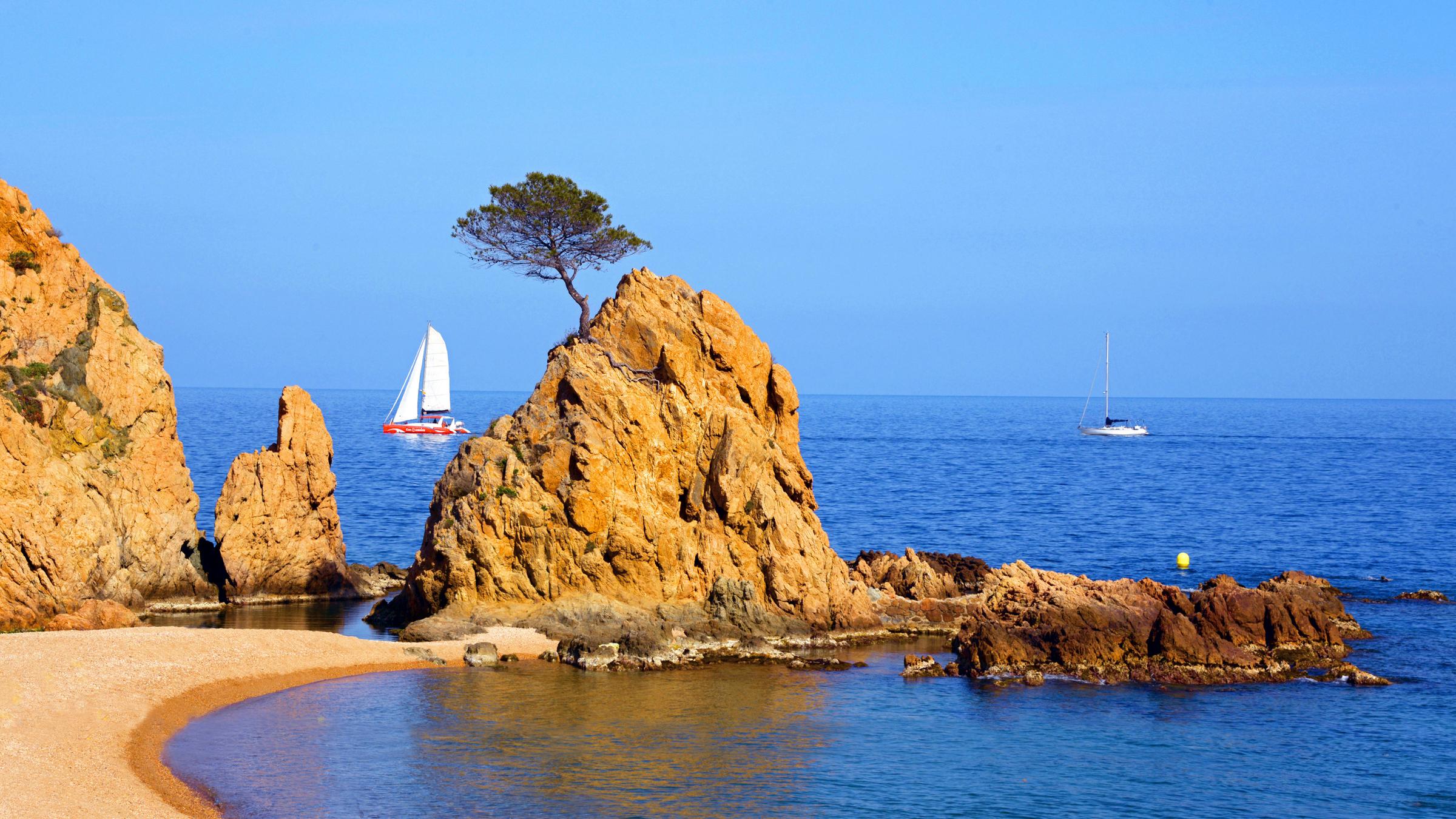 Am Strand ragt ein kleiner Felsen ins Wasser. Es ist tolles sonniges Wetter.