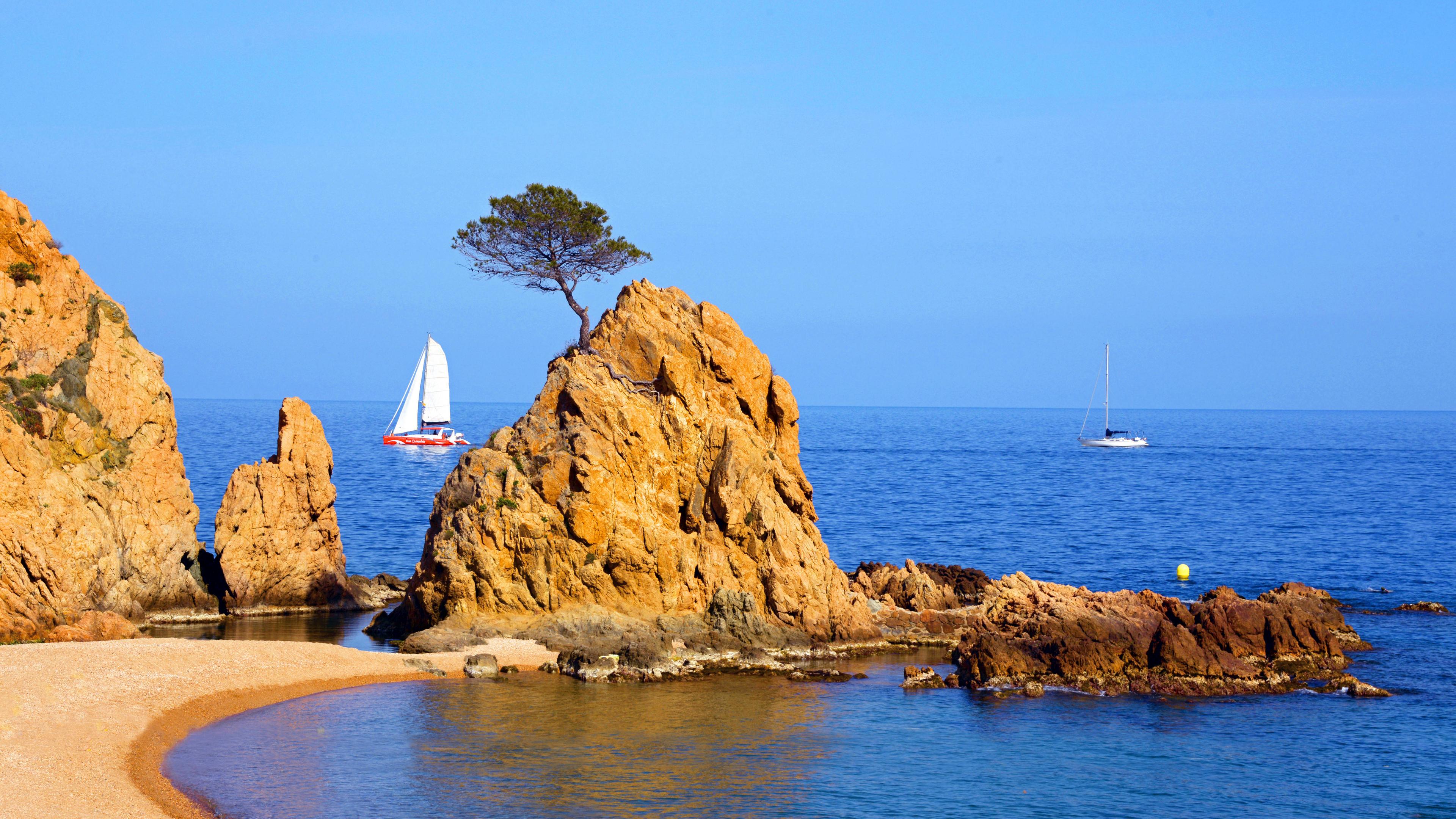Am Strand ragt ein kleiner Felsen ins Wasser. Es ist tolles sonniges Wetter.