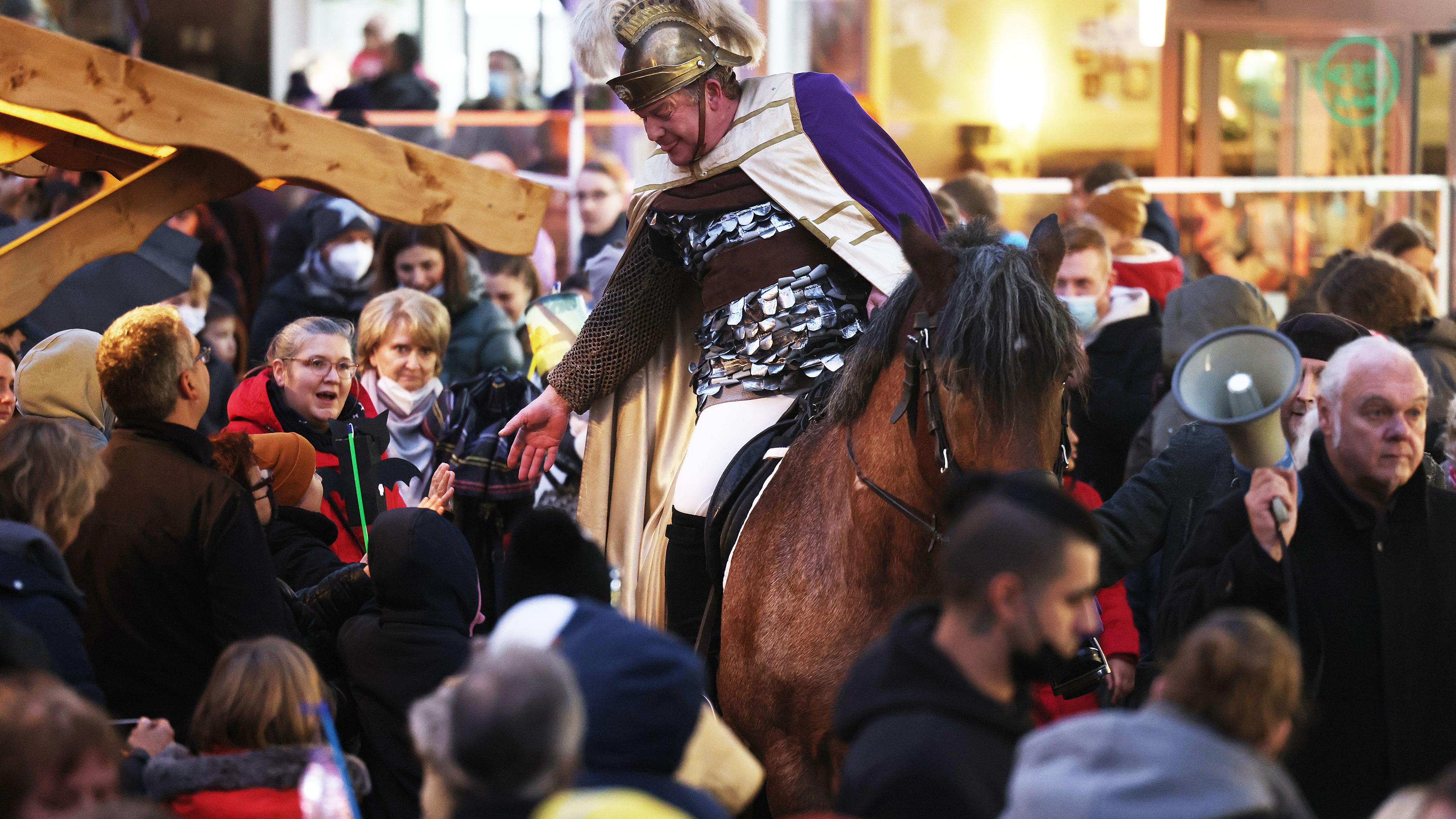 Kinder gehen in der Dämmerung mit Laternen spazieren, vorneweg reitet jemand als St. Martin verkleidet.