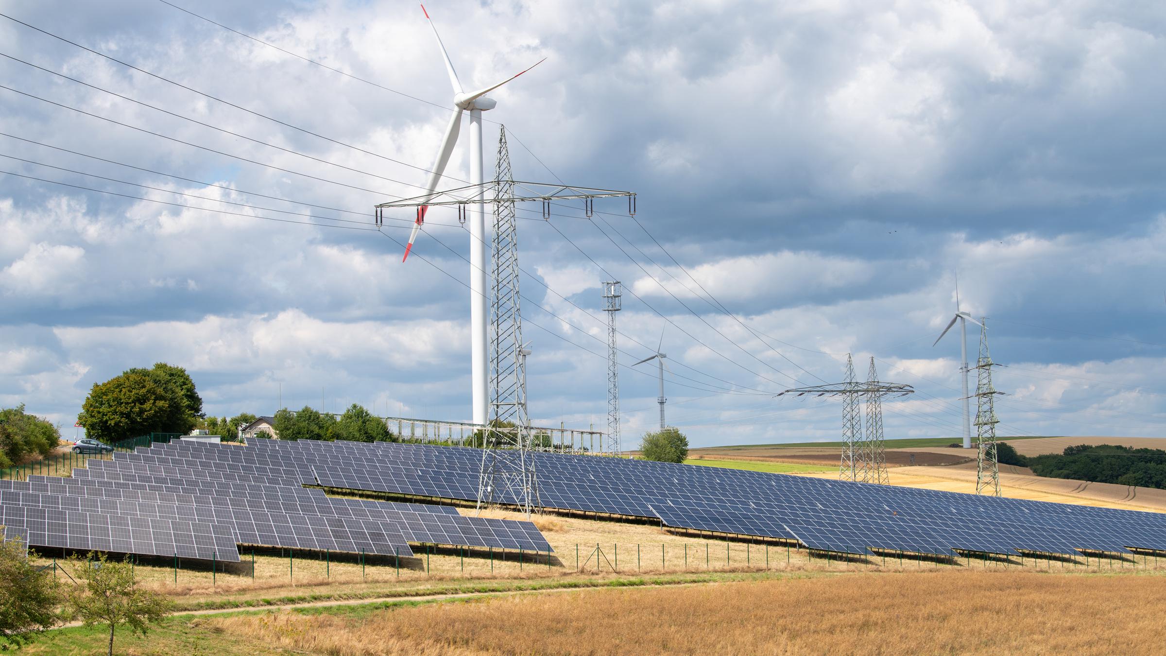 Landwirtschaftliches Feld mit Windrädern und Solarzellenstation.