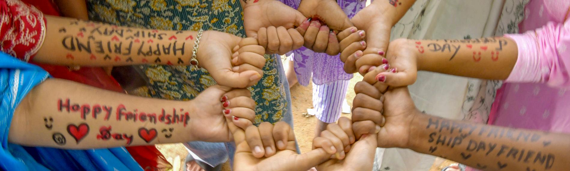 Eine Gruppe indischer Schülerinnen steht im Kreis und hält sich in den Händen. Auf ihre Unterarme haben sie "Happy Friendship Day", also "Fröhlichen Tag der Freundschaft" geschrieben.