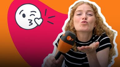 Vor einem rot-orangenen Hintergrund ist Reporterin Lara mit Mikrofon zu sehen. Sie macht einen Kussmund in die Kamera. Neben ihr befindet sich ein Kuss-Emoji.