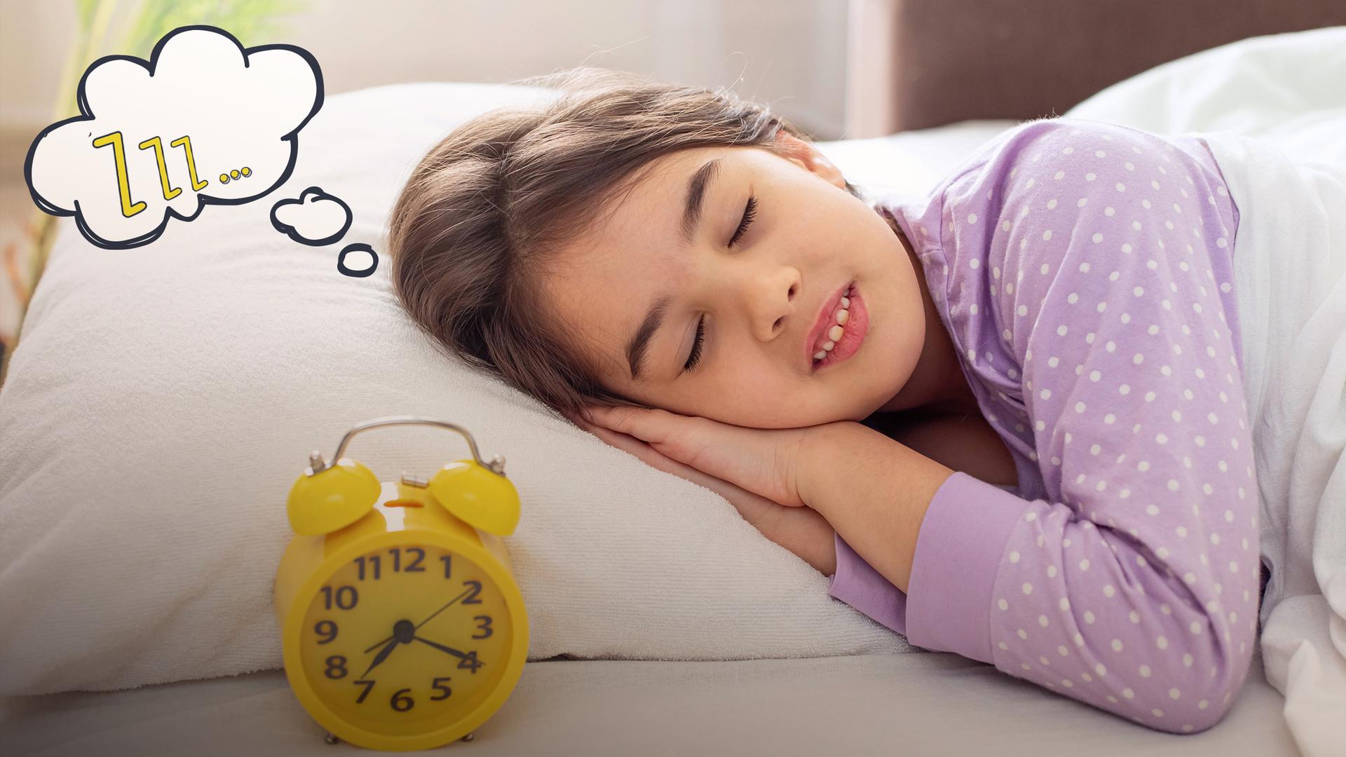 Ein schlafendes brünettes Mädchen in einem lila gepunkteten Schlafanzug liegt auf einem weißen Kissen.