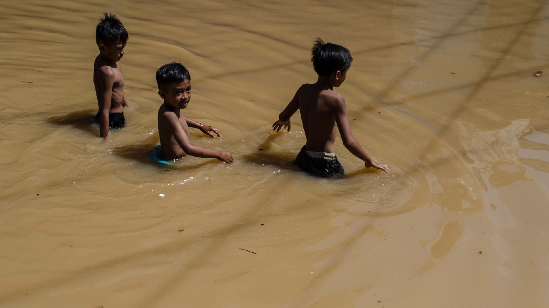 Drei Kinder waten durch Hochwaser. Symbolbild