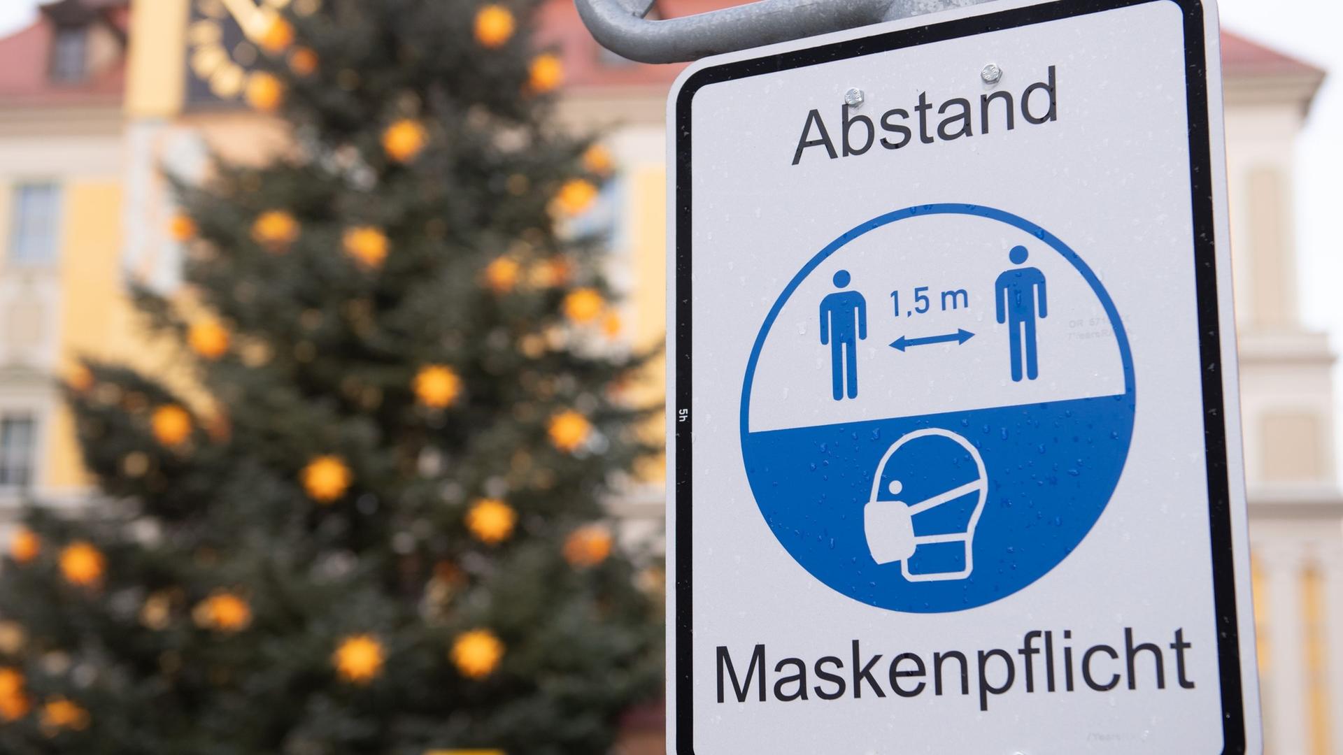 Ein Hinweisschild für die Maskenpflicht vor einem Weihnachtsbaum.