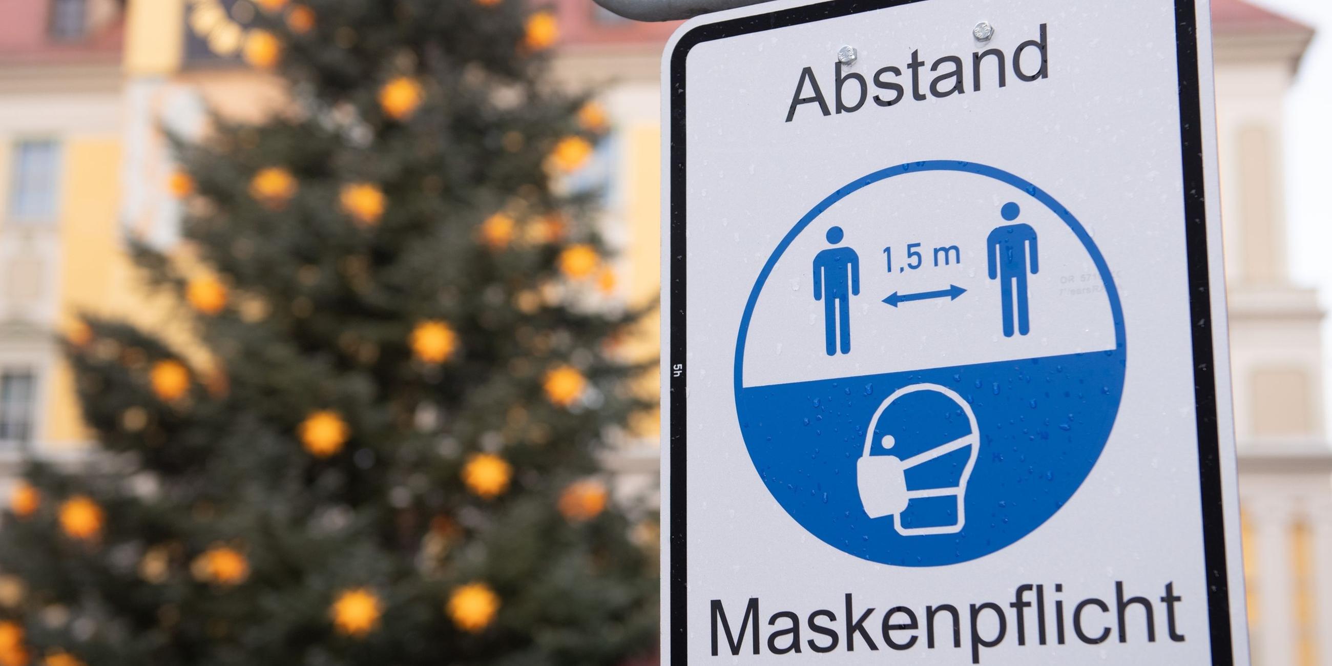 Ein Hinweisschild für die Maskenpflicht vor einem Weihnachtsbaum.