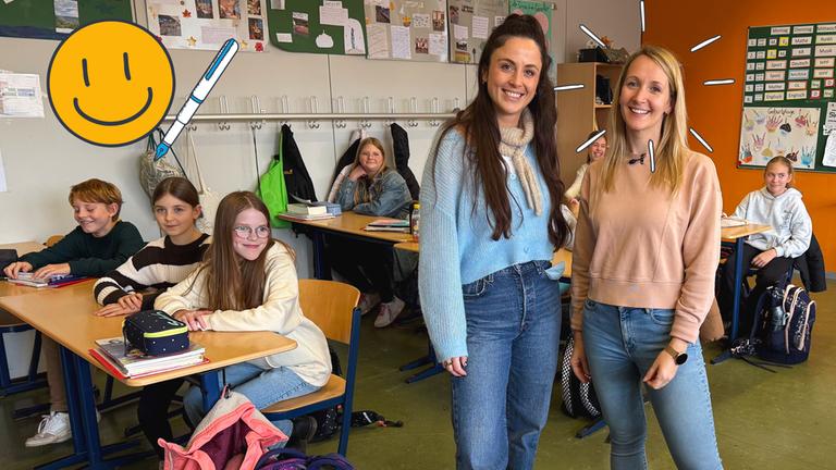 Reporterin Teresa steht neben Frau Jücker, eine Lehrerin an der IGS in Nieder-Olm. Sie stehen in einer Klasse, in der Kinder an Tischen sitzen und in die Kamera lächeln.