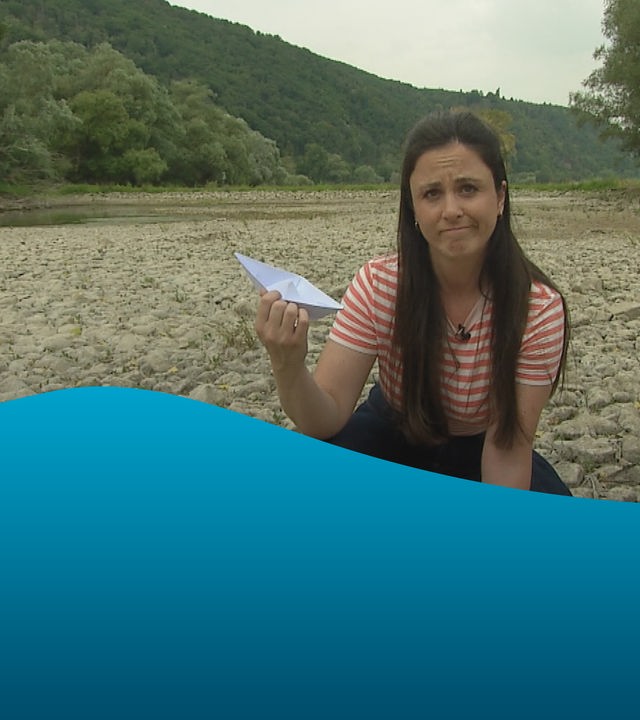 Teresa sitzt mit Papierschiffchen in der Hand auf ausgetrocknetem Rheinboden