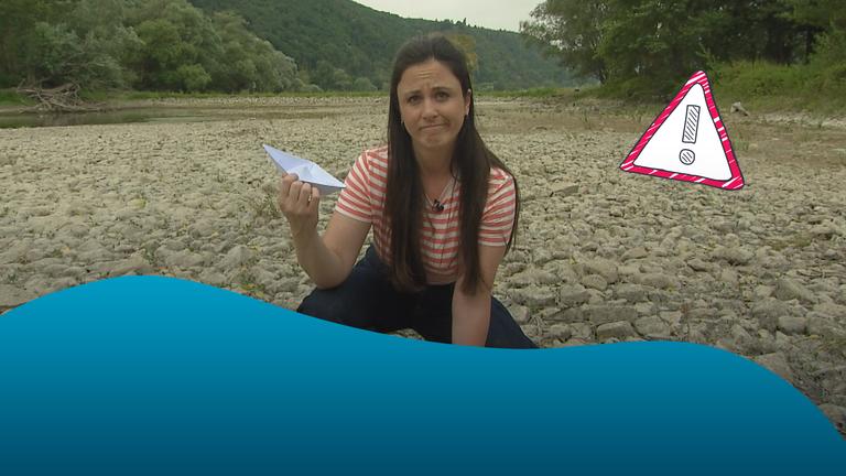 Teresa sitzt mit Papierschiffchen in der Hand auf ausgetrocknetem Rheinboden