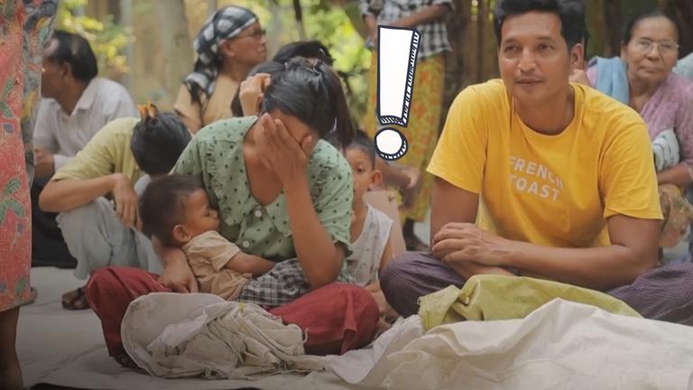 Menschen sitzen auf Boden, darunter eine Frau, die sich Hand vor das Gesicht hält und Baby im Arm hat