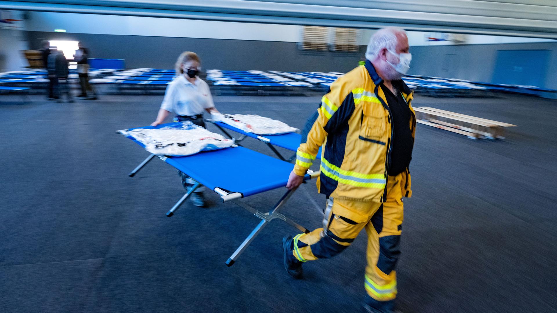 18.03.2022, Mecklenburg-Vorpommern, Greifswald: Helfer von DRK, THW und Feuerwehr wandeln in Greifswald eine Sporthalle in eine Notunterkunft für Flüchtlinge aus der Ukraine um. Es wurden Matten auf dem Boden verlegt und Feldbetten aufgestellt, wie der Landkreis Vorpommern-Greifswald mitteilte. In der erst vor wenigen Monaten fertiggestellten Halle können demnach nun bis zu 200 Flüchtlinge unterkommen. Foto: Stefan Sauer/dpa +++ dpa-Bildfunk +++