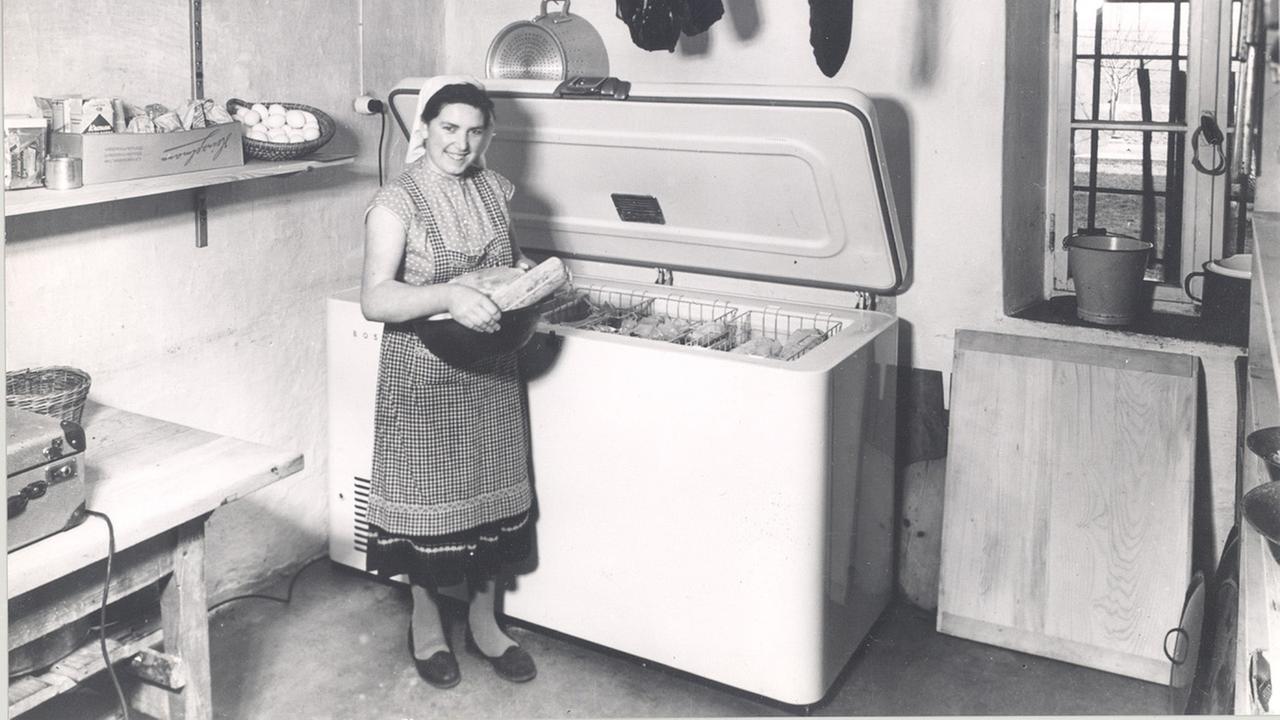Eine Frau steht auf einem schwarz-weiß-Foto vor eine Tiefkühltruhe.