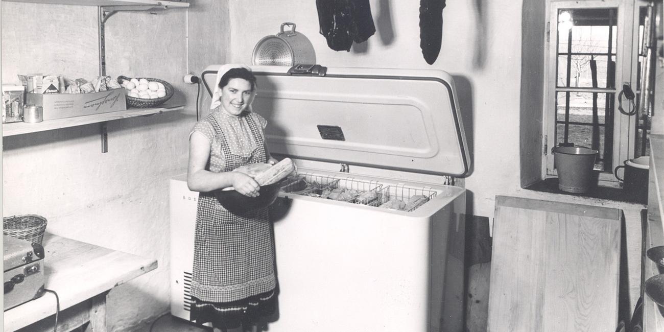 Eine Frau steht auf einem schwarz-weiß-Foto vor eine Tiefkühltruhe.
