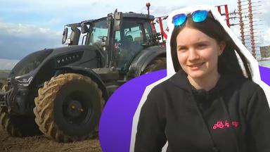 Eine junge Frau im schwarzen Pulli, im Hintergrund ein riesiger Traktor. 