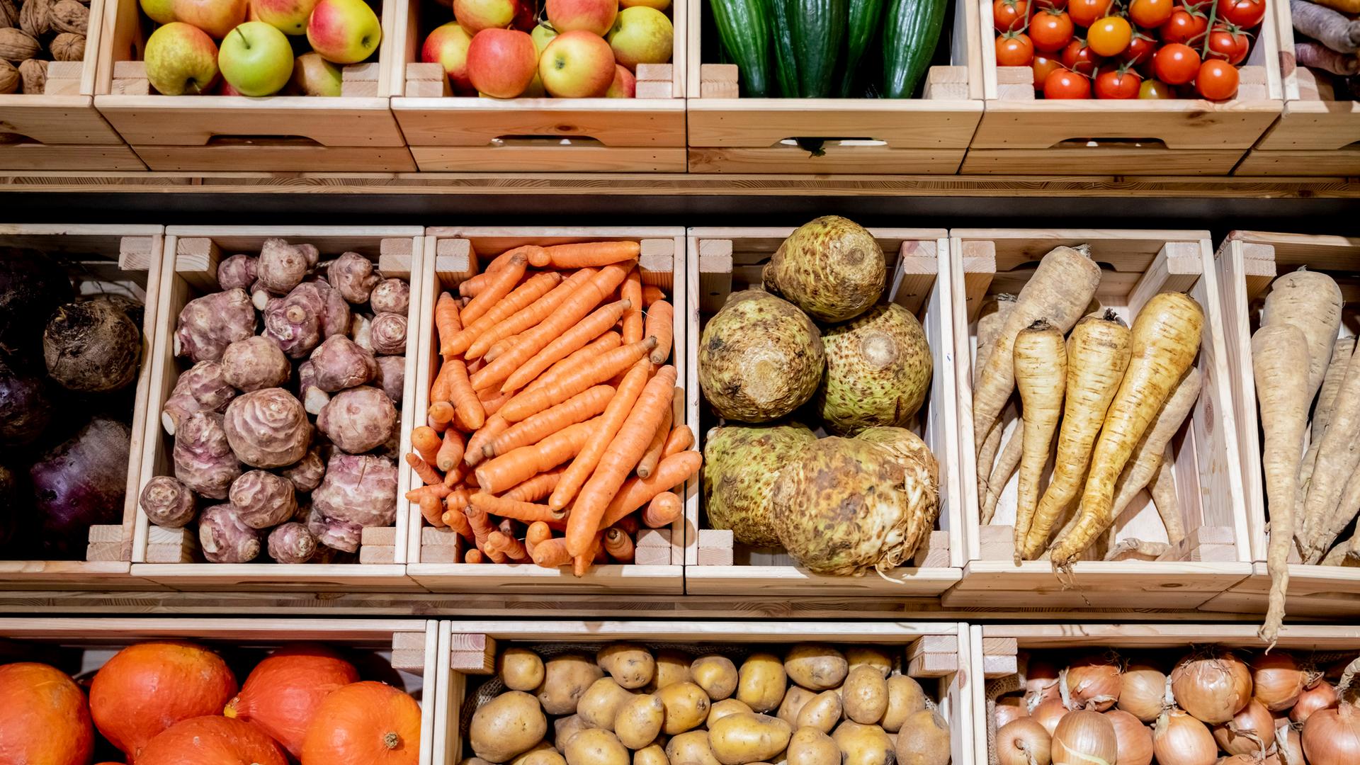 Auf dem Foto sieht man Obst und Gemüse in einem Supermarkt. Es ist auf Holzkisten verteilt und sieht sehr appetitlich aus. 