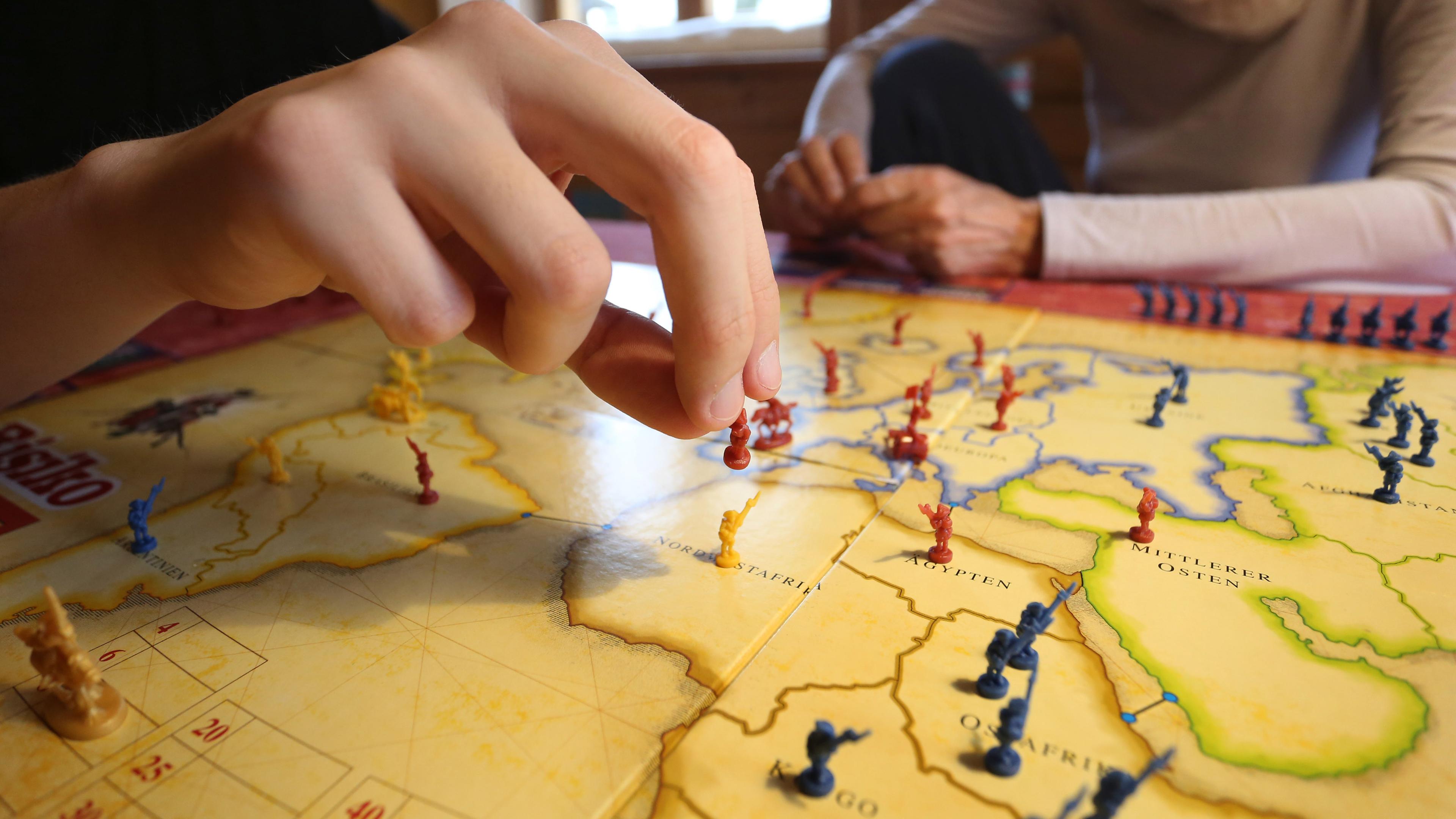 Auf dem Bild sieht man eine Hand und ein Spielbrett. Die Hand versetzt gerade eine Spielfigur.