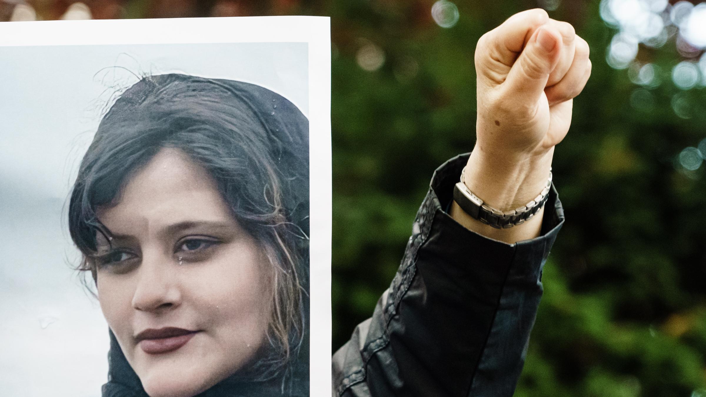 Jemand hält das Foto der verstorbenen Mahsa Amini und reckt seine Faust daneben in die Luft.
