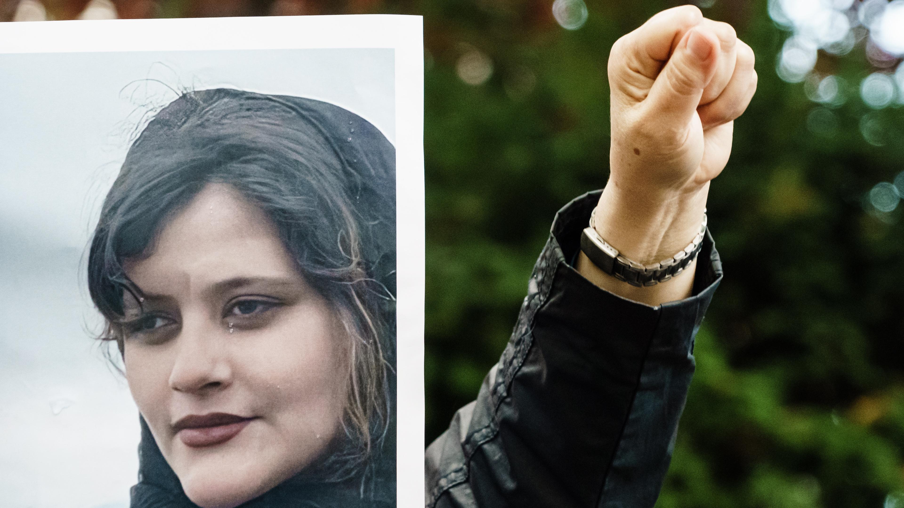Jemand hält das Foto der verstorbenen Mahsa Amini und reckt seine Faust daneben in die Luft.