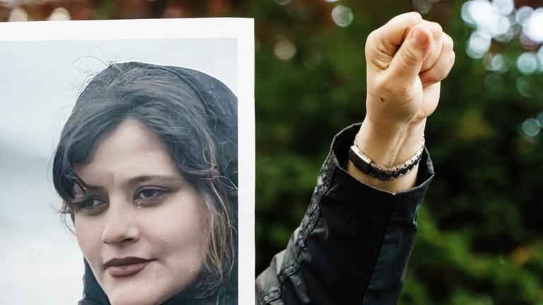 Jemand hält das Foto der verstorbenen Mahsa Amini und reckt seine Faust daneben in die Luft.