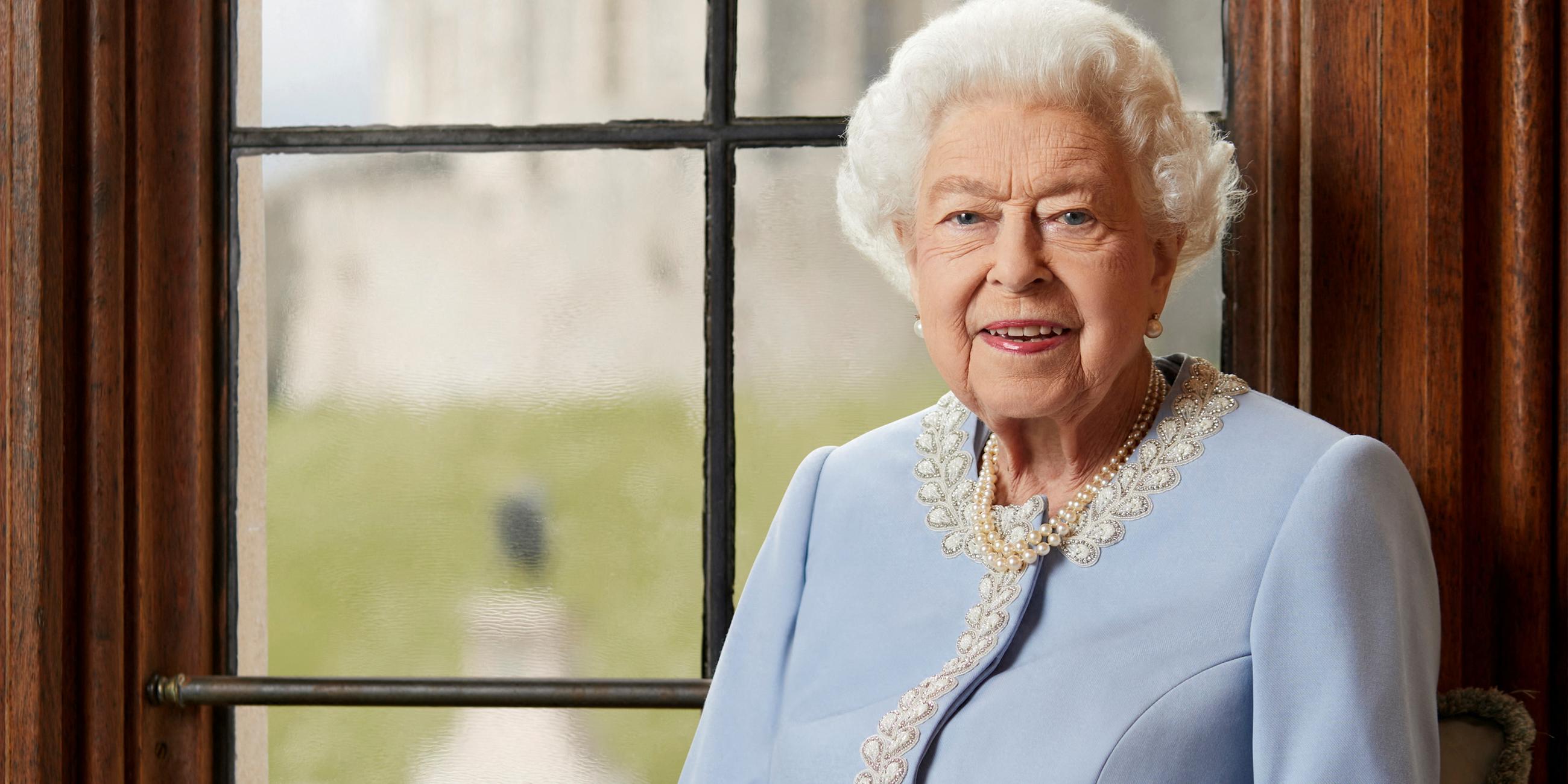 Rot uniformierte Sargträger tragen den blumenverzierten Sarg der verstorbenen Queen Elizabeth II vor schwarzem Hintergrund. Oben prangt eine Krone. 