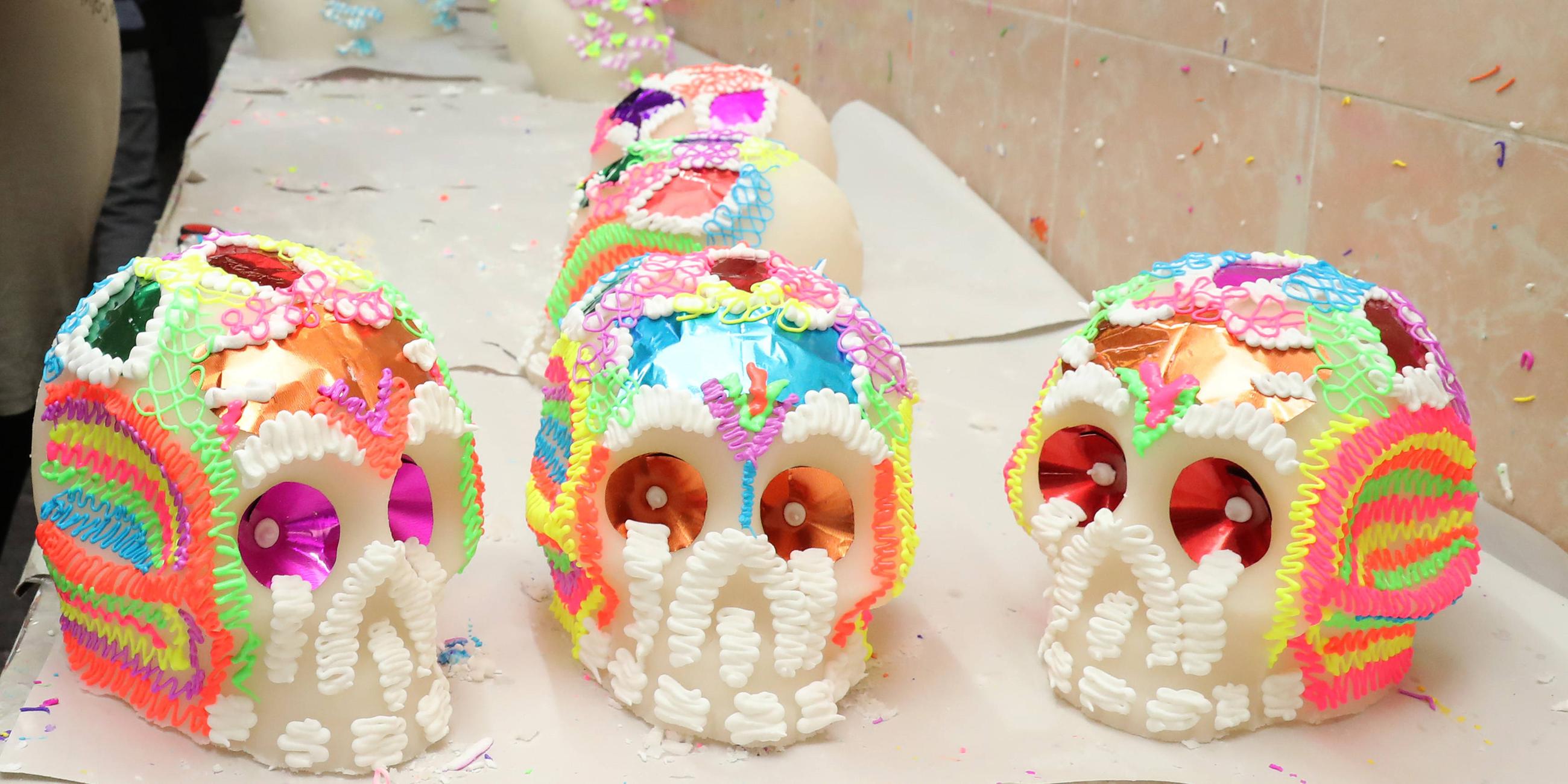 Ein Mann verziert Süßigkeiten in Totenkopfform mit bunten Zuckermustern.