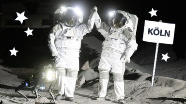 Zwei Astronauten geben sich High-Five, daneben steht ein Schild mit dem Wort Köln