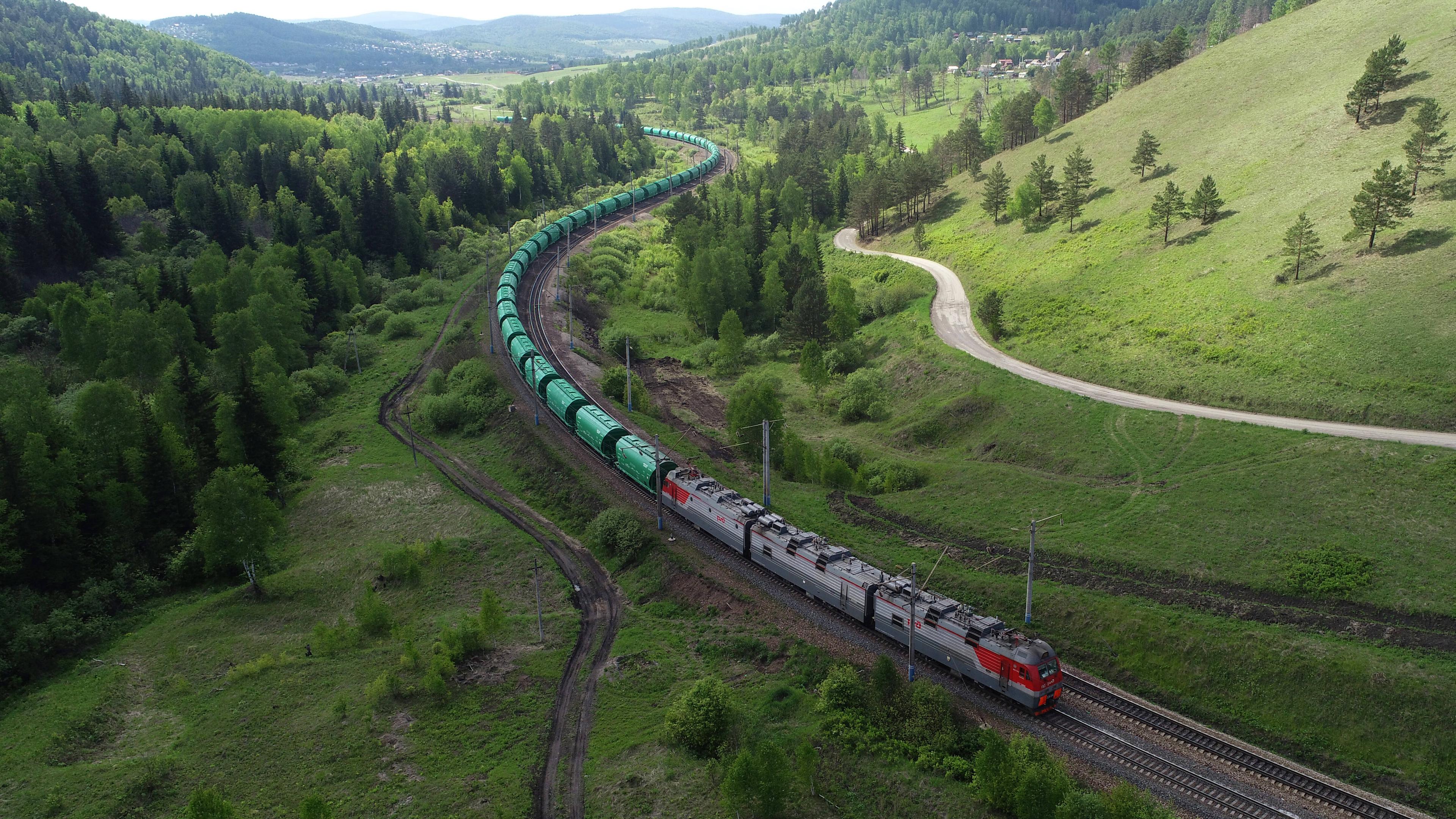 Die Transsibirische Eisenbahn, die durch eine grüne, hügelige Landschaft fährt. 