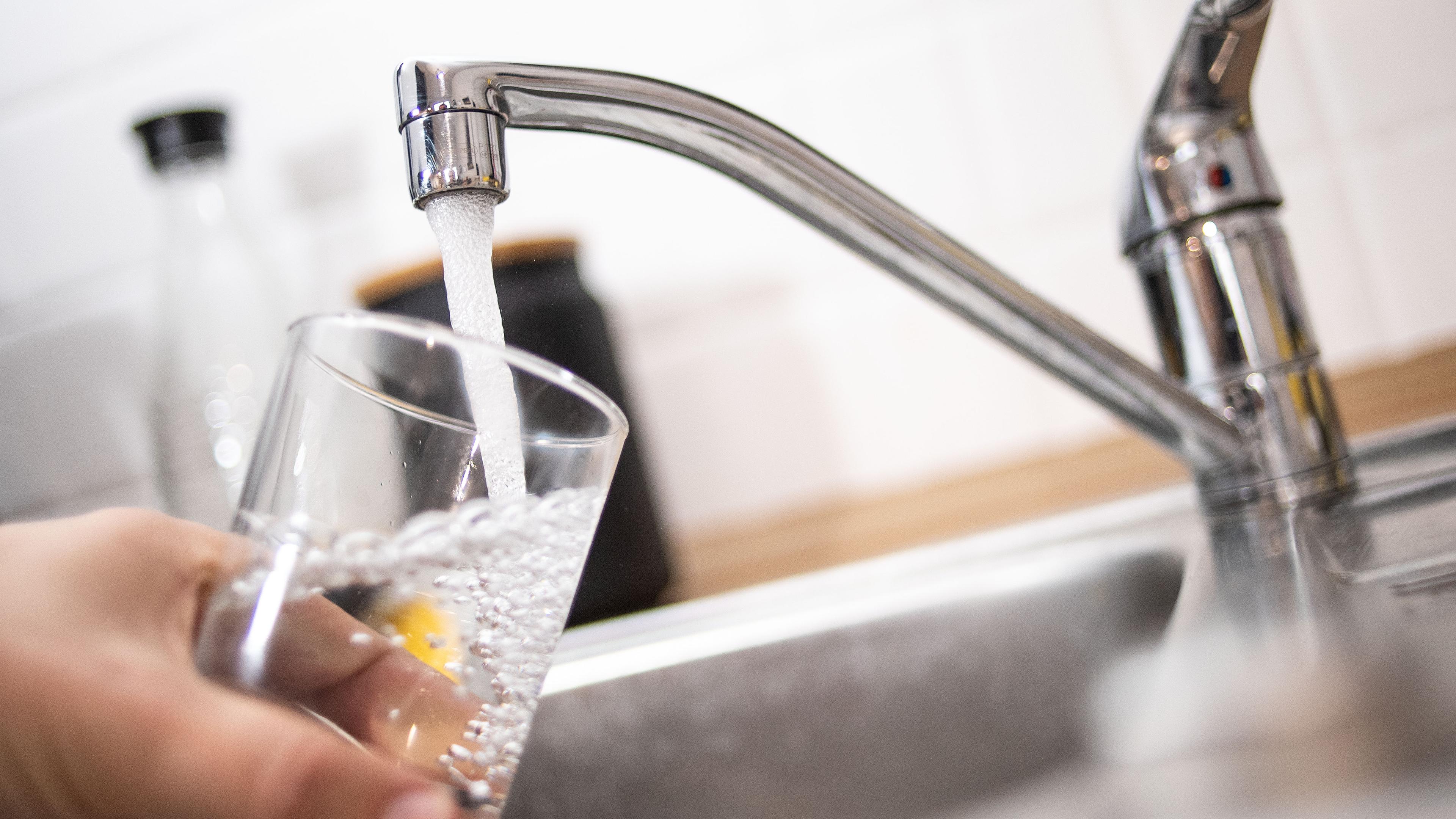 Ein Mann haelt ein Glas unter einen laufenden Wasserhahn.
