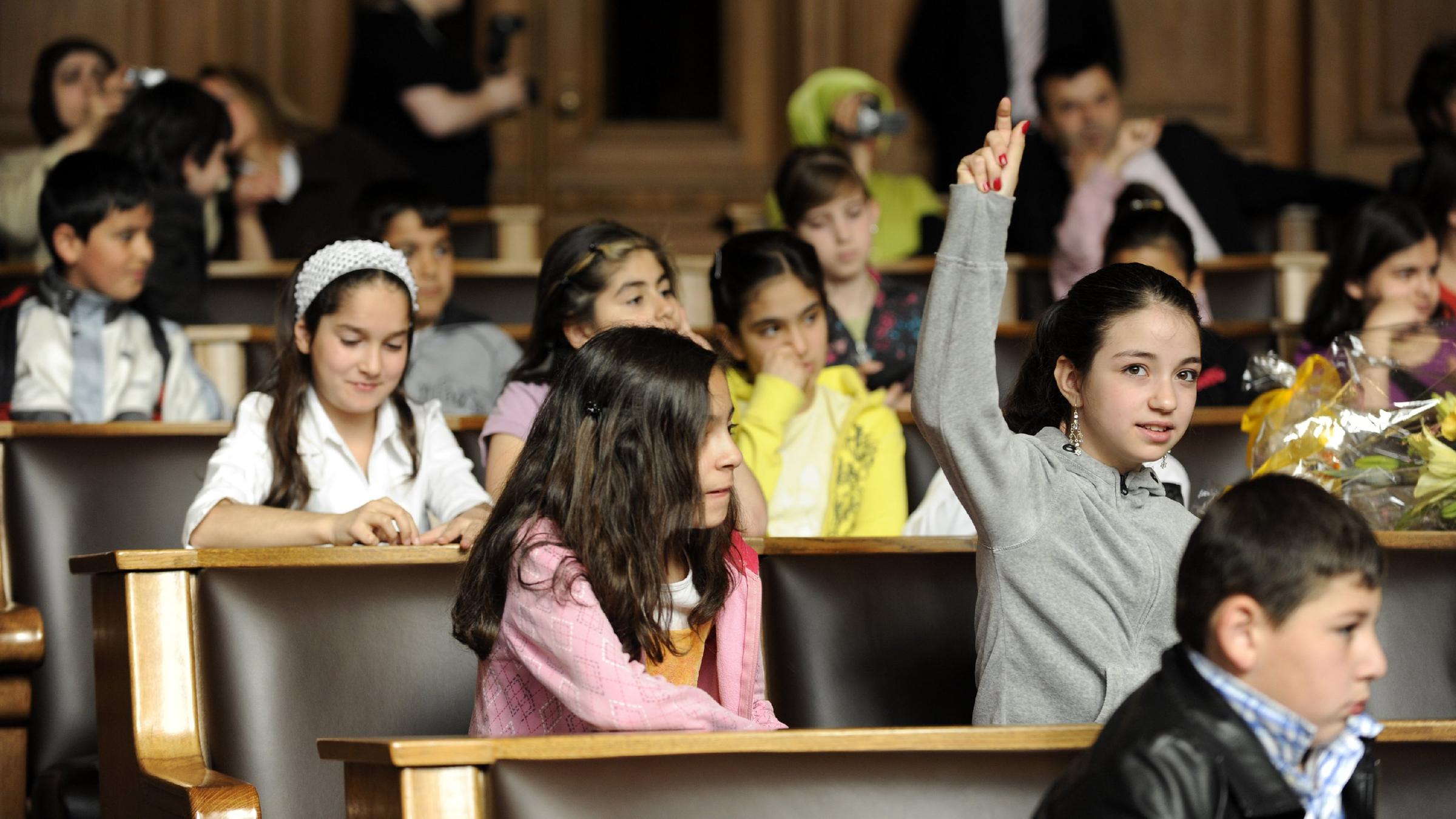 Kinder sitzen nebeneinander und melden sich