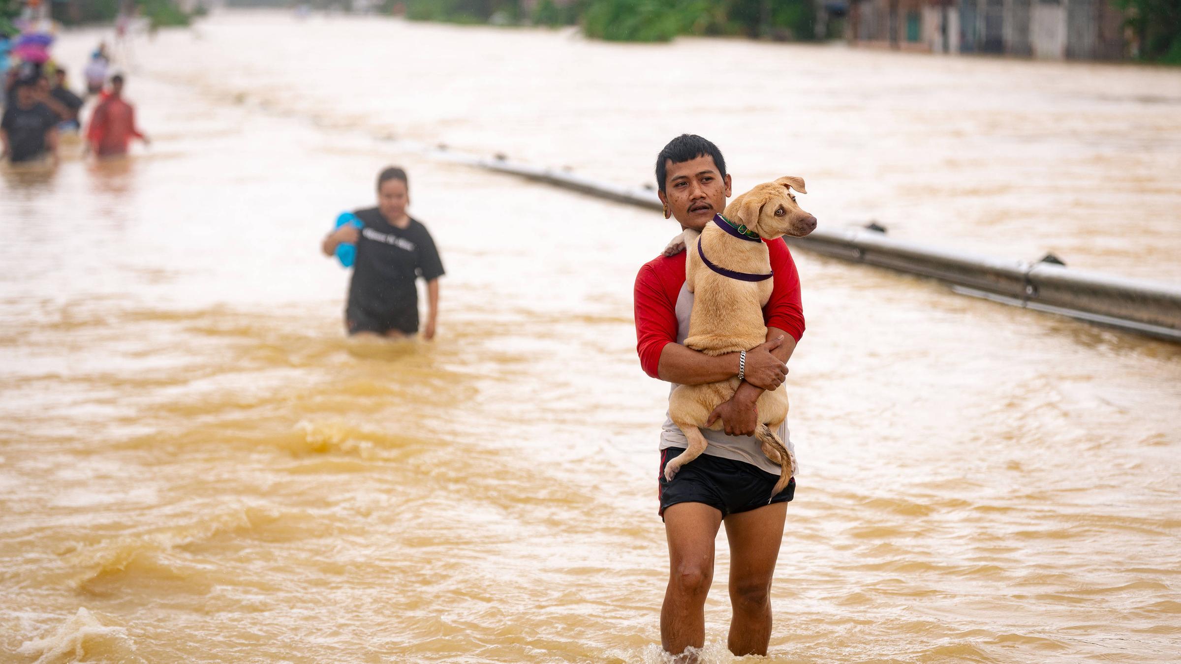 Viele Menschen müssen durch das Wasser laufen. Ein Mann trägt seinen Hund im Arm.