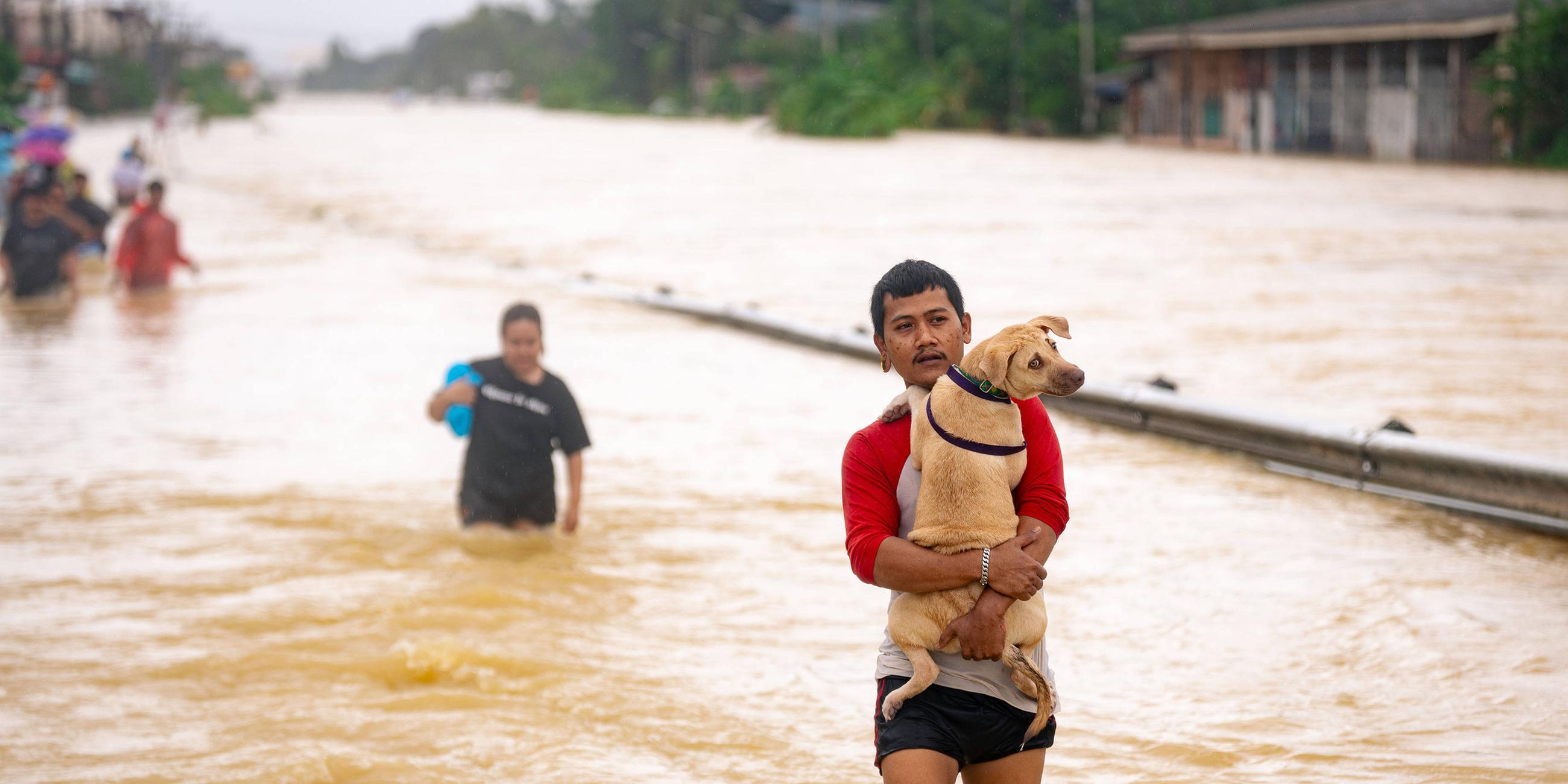Viele Menschen müssen durch das Wasser laufen. Ein Mann trägt seinen Hund im Arm.