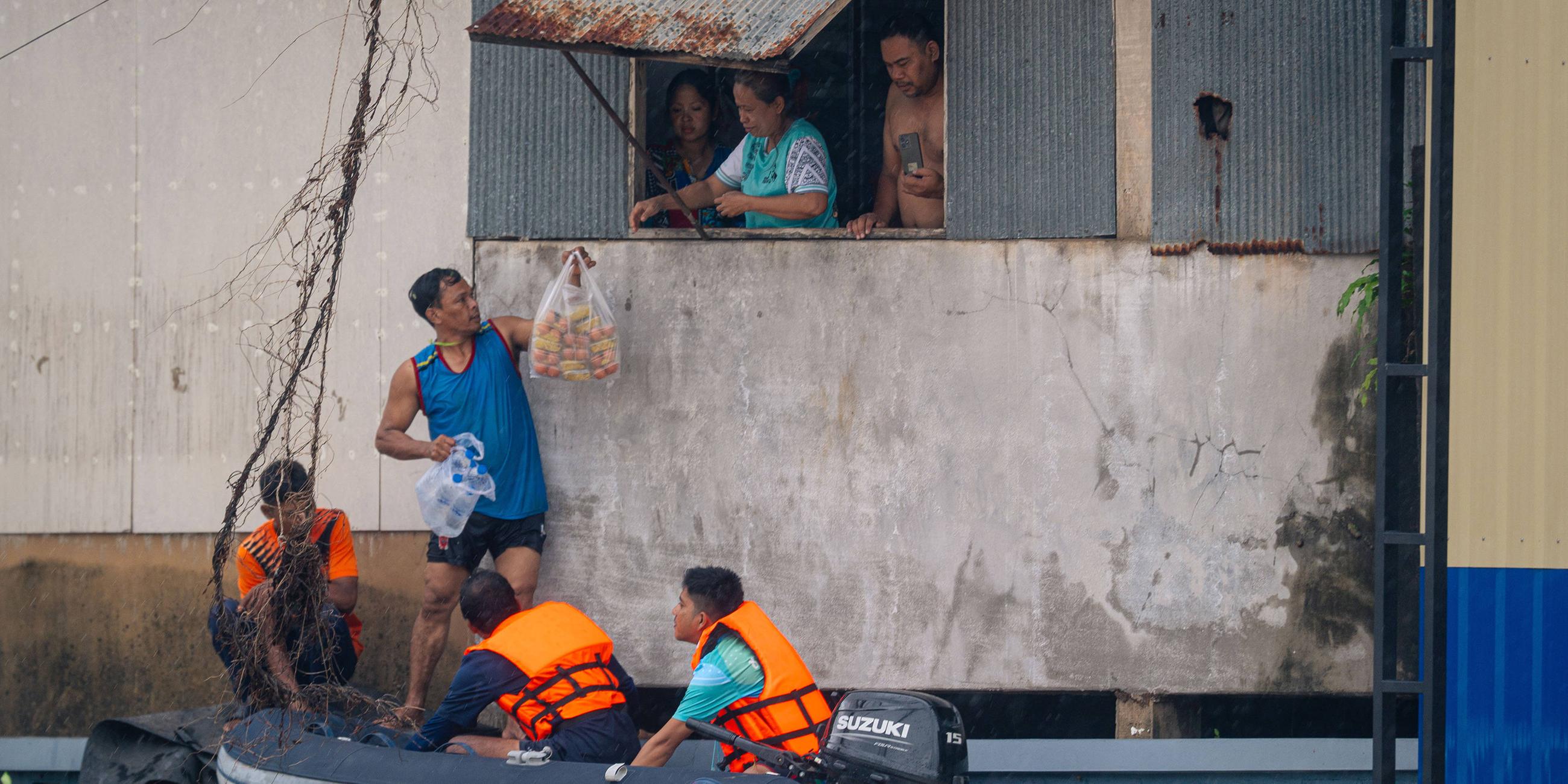 Anwohner sind durch das Wasser in ihren Häusern gefangen. Deshalb bekommen sie Essen von Helfern.
