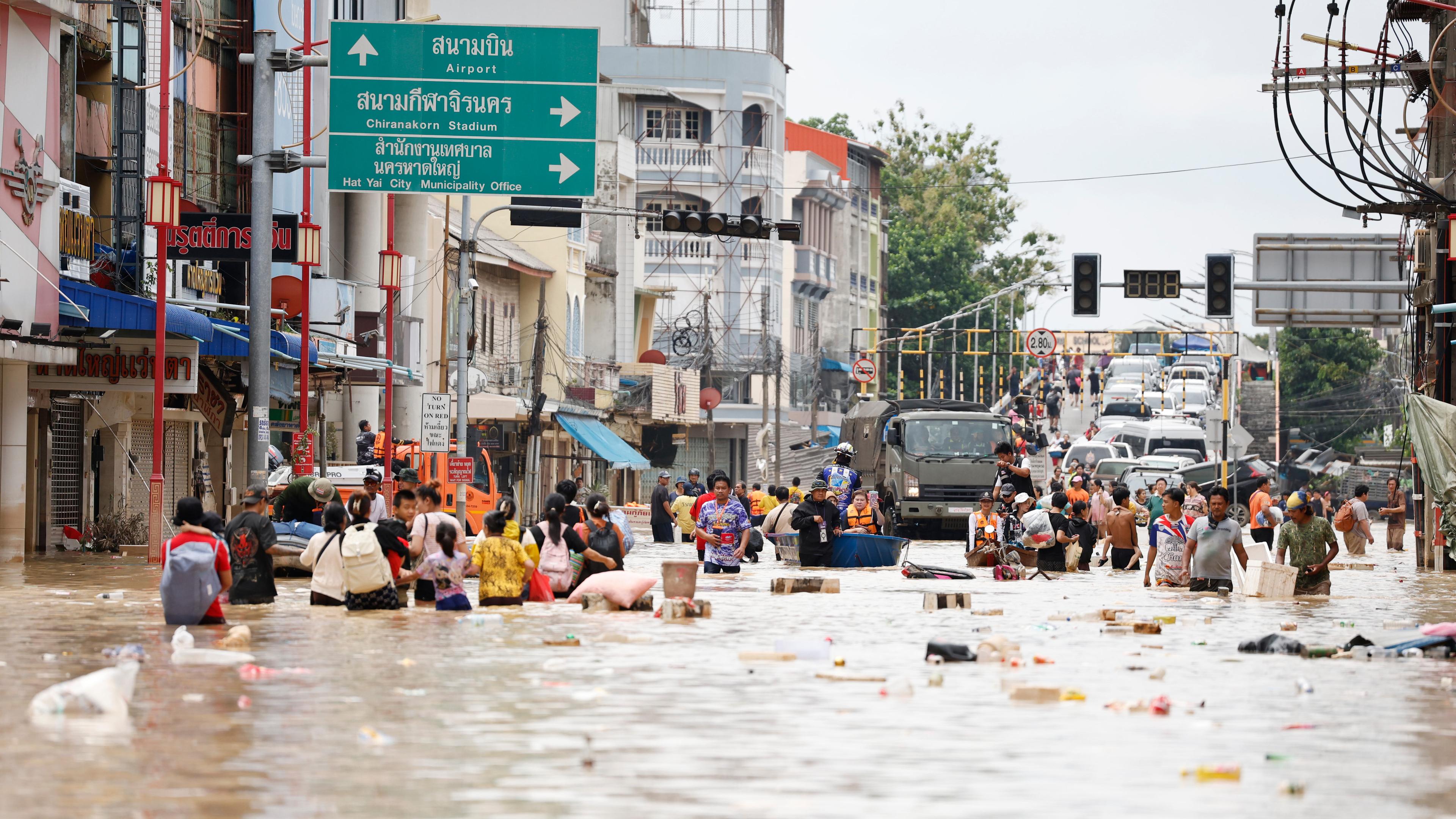 Menschen laufen durch das Hochwasser im Gebiet Songkhla. Überall schwimmen Gegenstände herum.