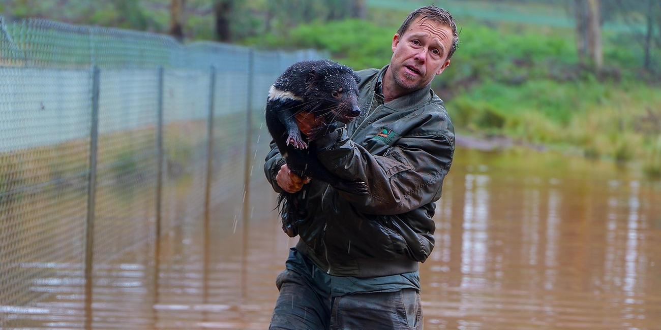 Mann steht im Hochwasser mit Hund auf Arm