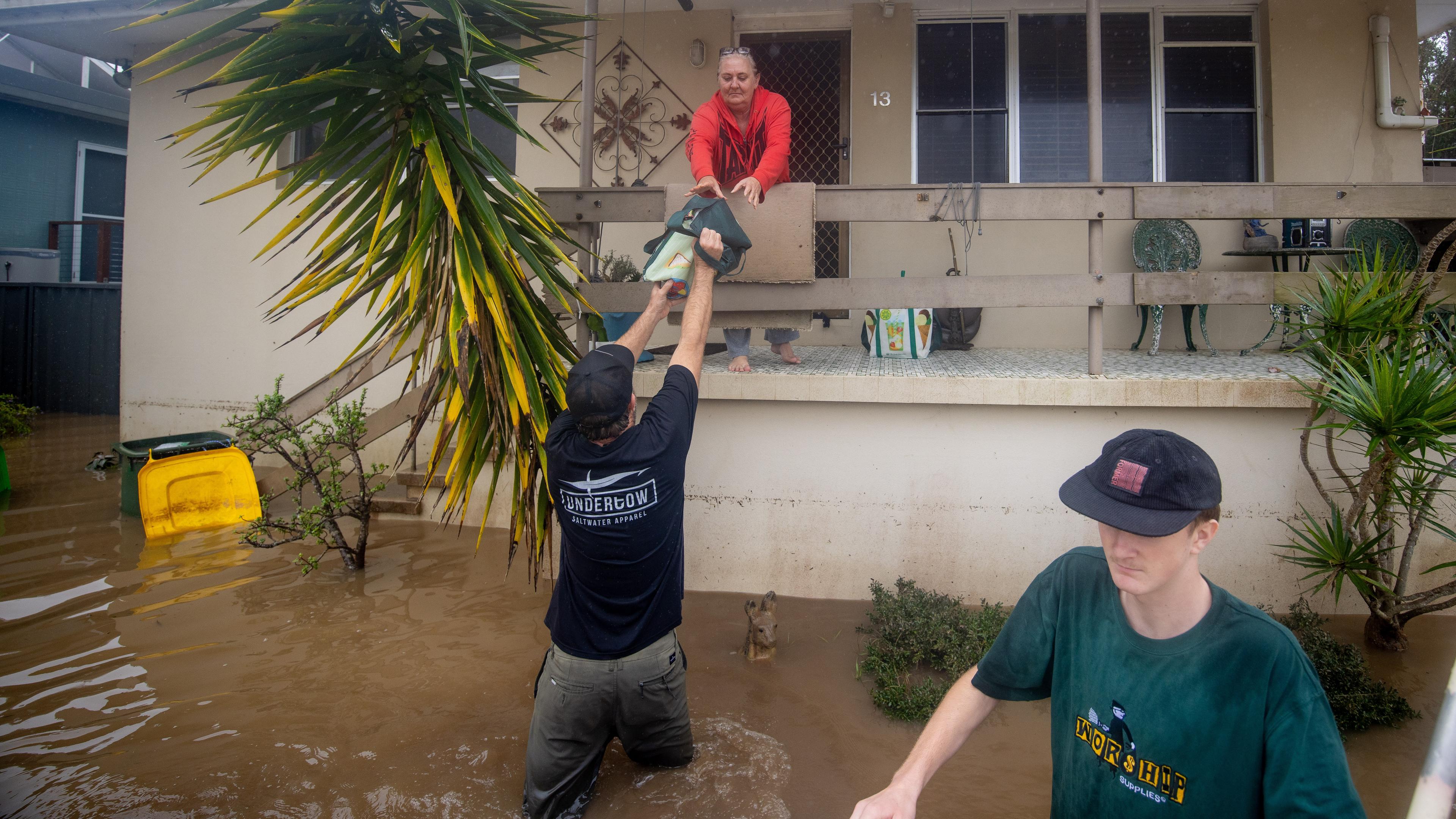 helfer stehen im Hochwasser und reichen Menschen, die in Häusern gefangen sind, Hilfslieferungen