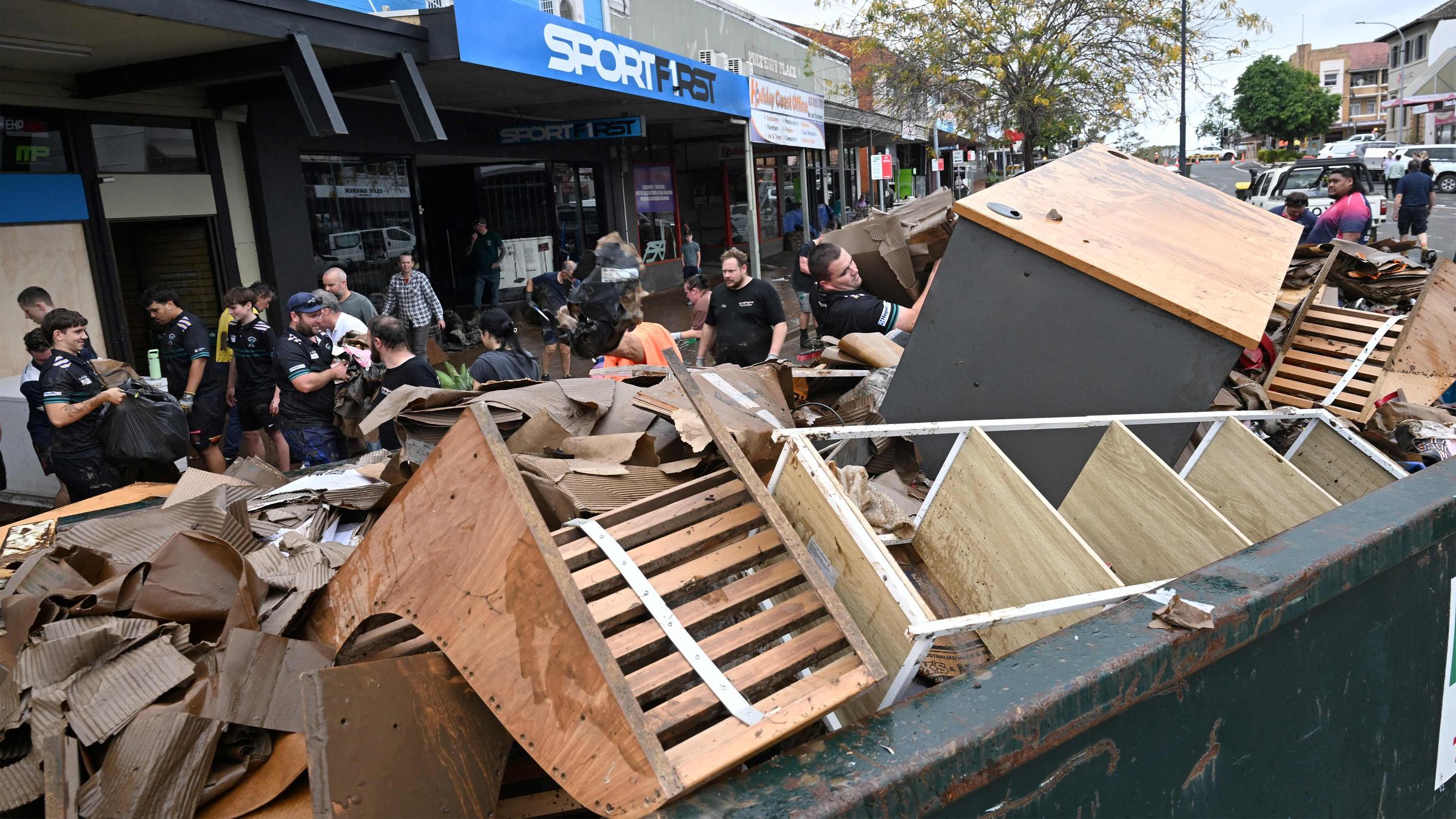 Zerstörte Möbel liegen in Container, Menschen packen Container voll