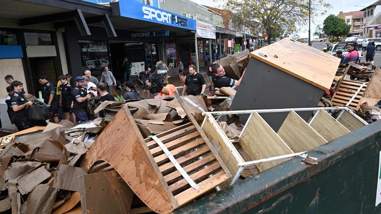 Zerstörte Möbel liegen in Container, Menschen packen Container voll