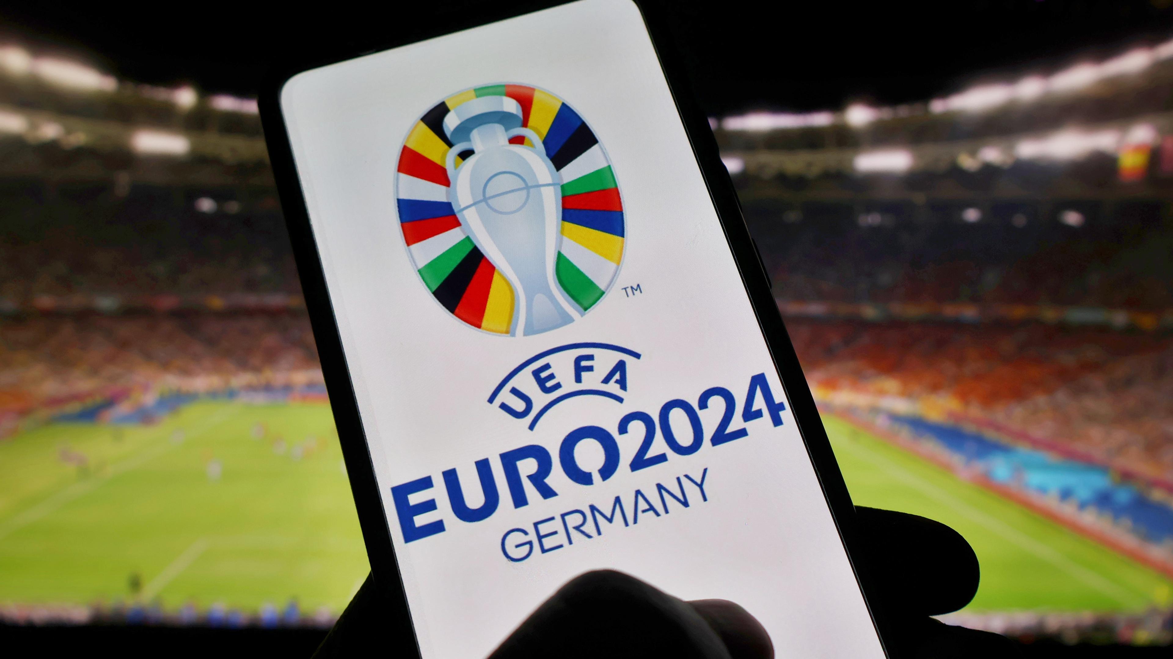 Handybildschirm, im Hintergrund ein Stadion. Auf Bildschirm ist Logo der EM 2024 zu sehen.