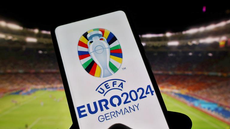 Handybildschirm, im Hintergrund ein Stadion. Auf Bildschirm ist Logo der EM 2024 zu sehen.