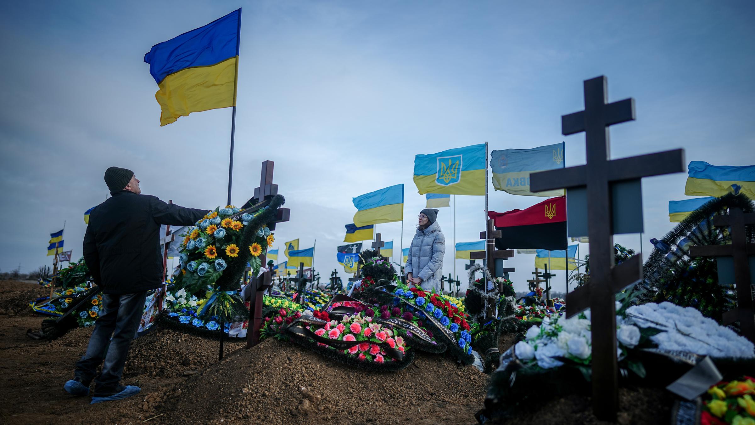 Ukraine, Odessa: Anna, die Ehefrau eines vor zwei Monaten getöteten Soldaten, und der Vater Oleksandr stellen auf dem Friedhof der Hafenstadt Odessa die Ukrainische Nationalflagge am Grab ihres Ehemannes auf.