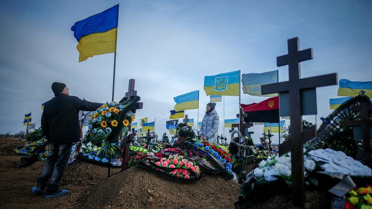 Ukraine, Odessa: Anna, die Ehefrau eines vor zwei Monaten getöteten Soldaten, und der Vater Oleksandr stellen auf dem Friedhof der Hafenstadt Odessa die Ukrainische Nationalflagge am Grab ihres Ehemannes auf.