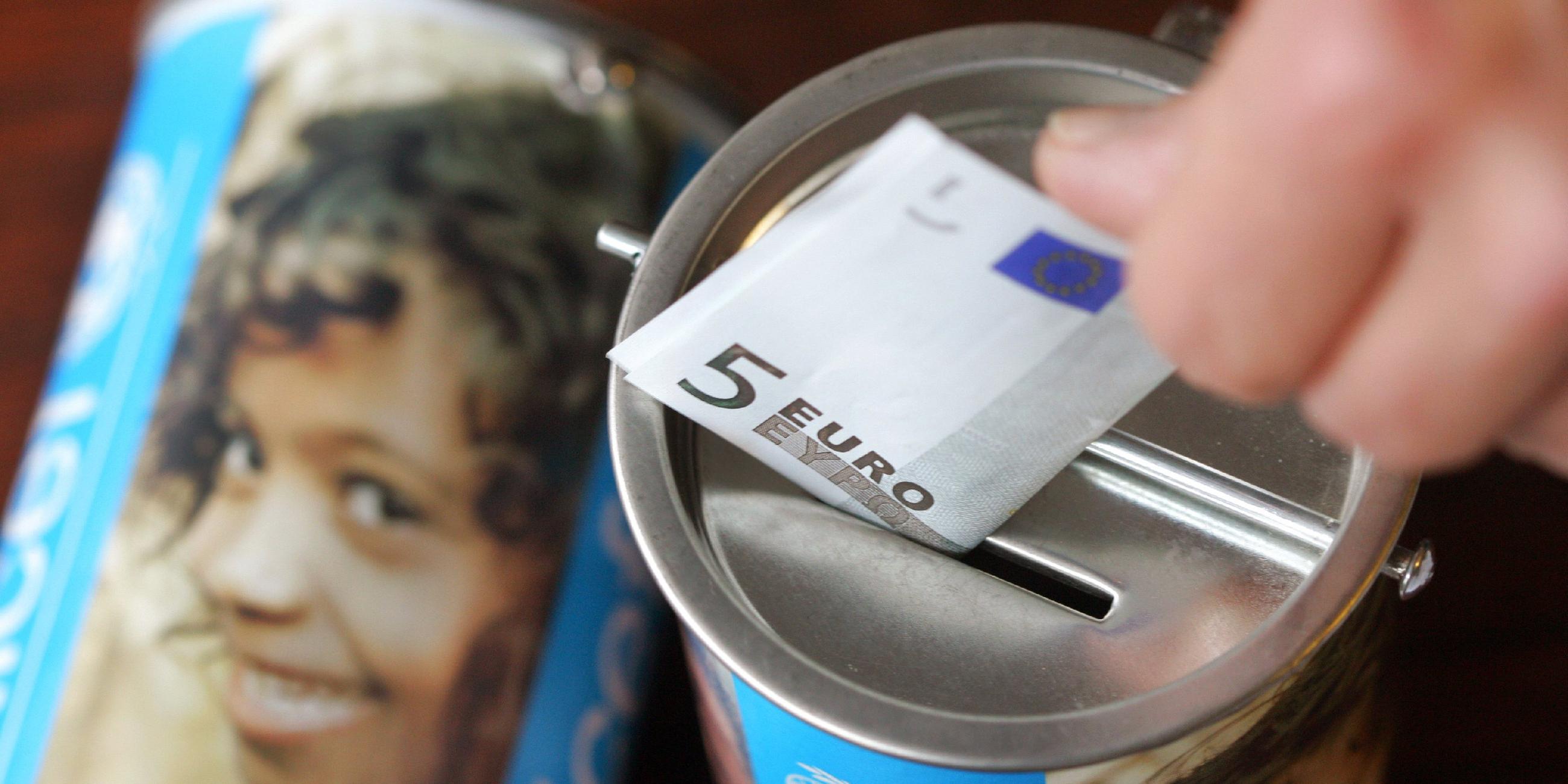 Eine Hand wirft einen Fünfeuroschein in eine Dose auf der Unicef steht